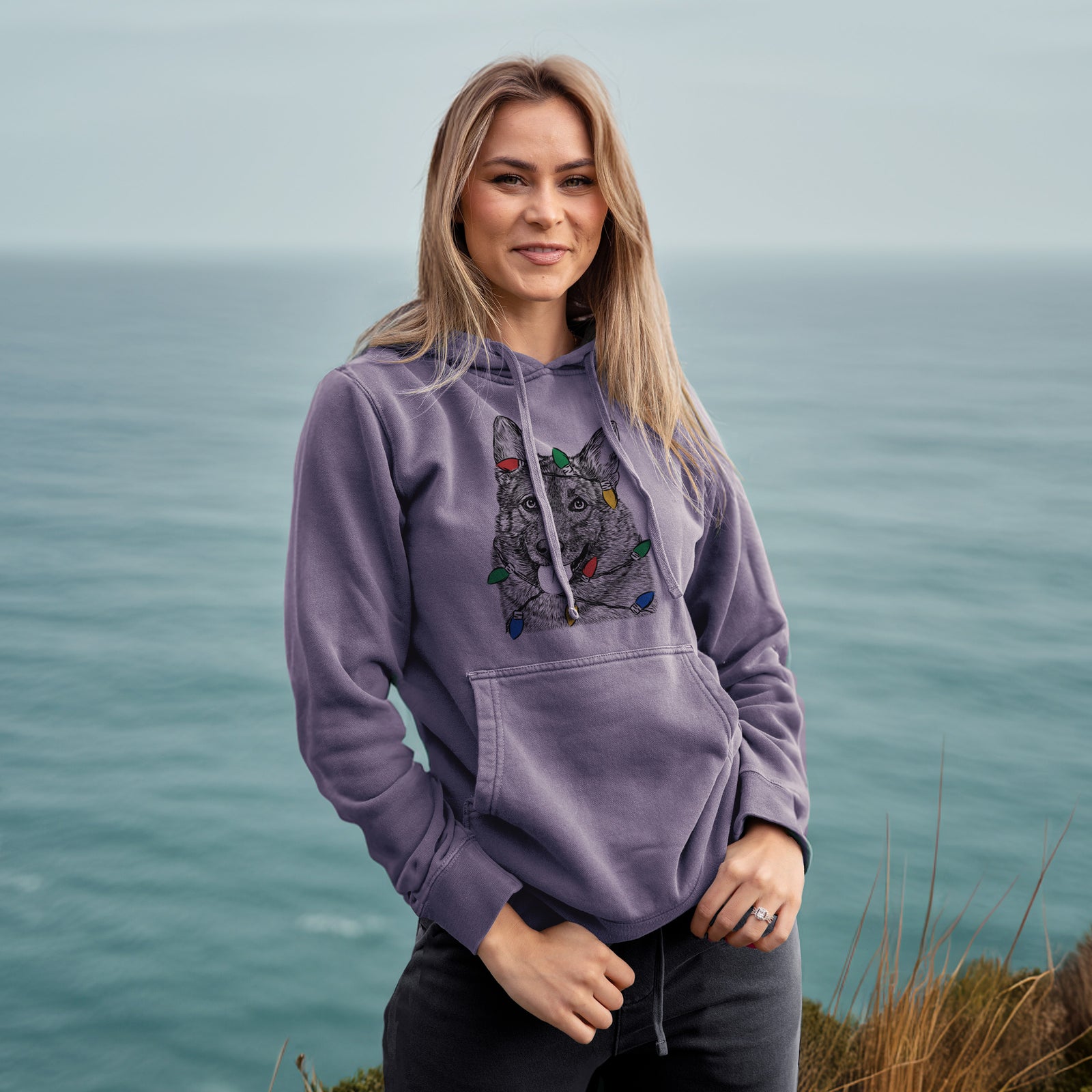 Hand-drawn sketch of Kasia the Norwegian Elkhound wrapped in Christmas lights on a Plum Unisex pigment dyed hoodie, worn by a woman