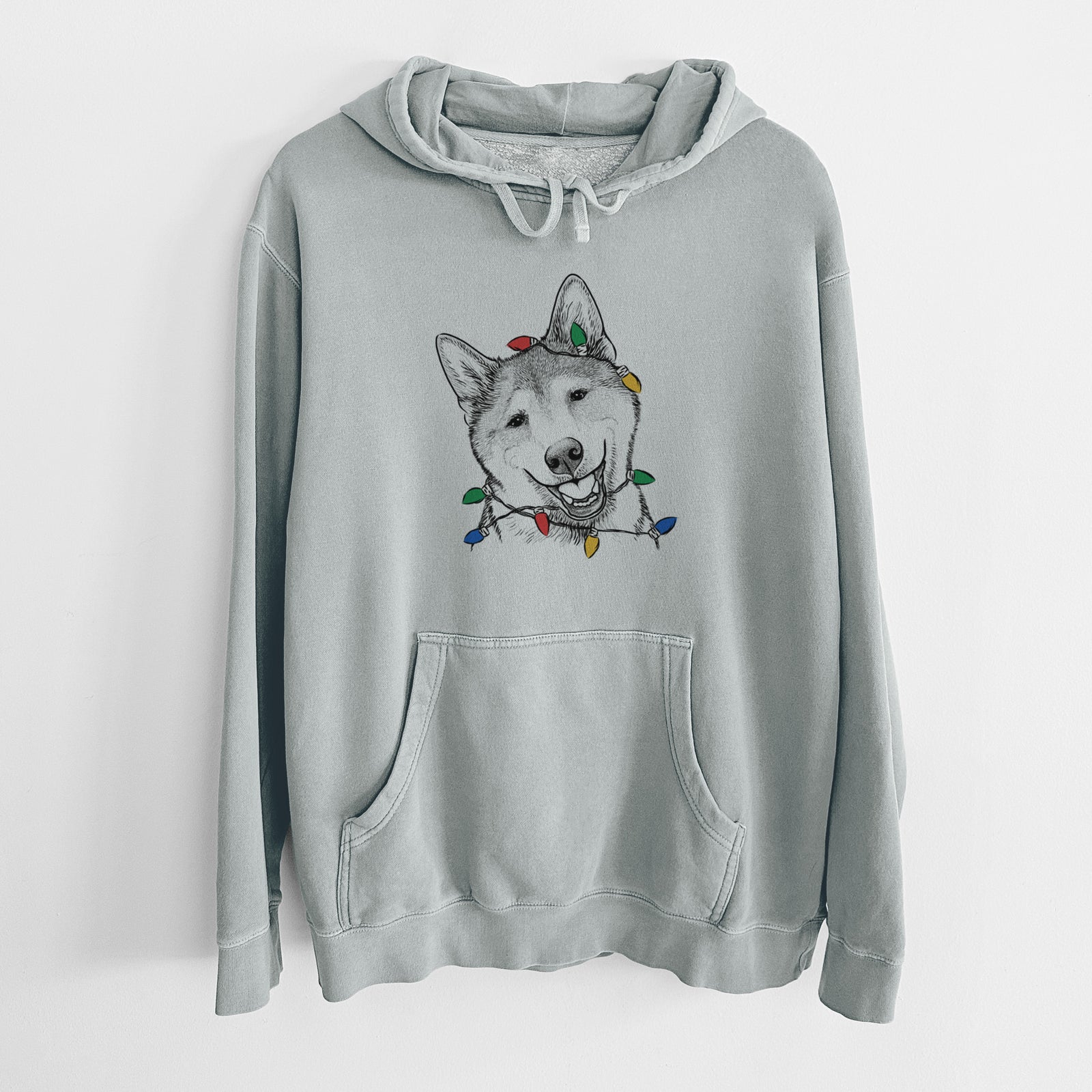 Hand-drawn sketch of Koby the Shiba Inu wrapped in Christmas lights on a Sage Unisex pigment dyed hoodie
