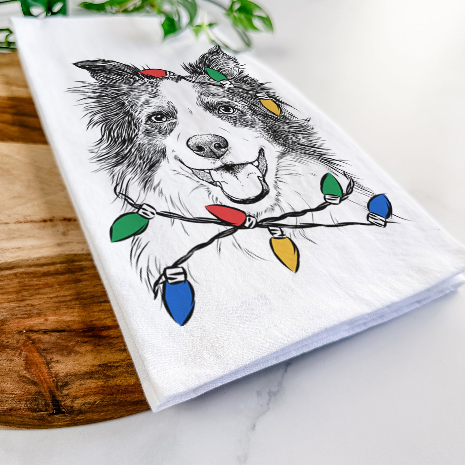 Hand-drawn sketch of Kylee the Border Collie wrapped in Christmas lights on a tea towel