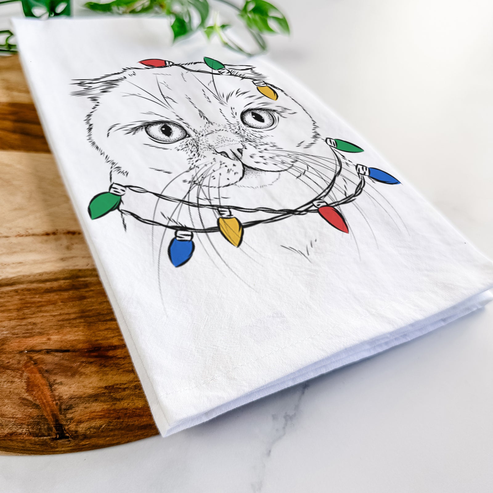 Hand-drawn sketch of Lina the Exotic Fold Cat wrapped in Christmas lights on a tea towel