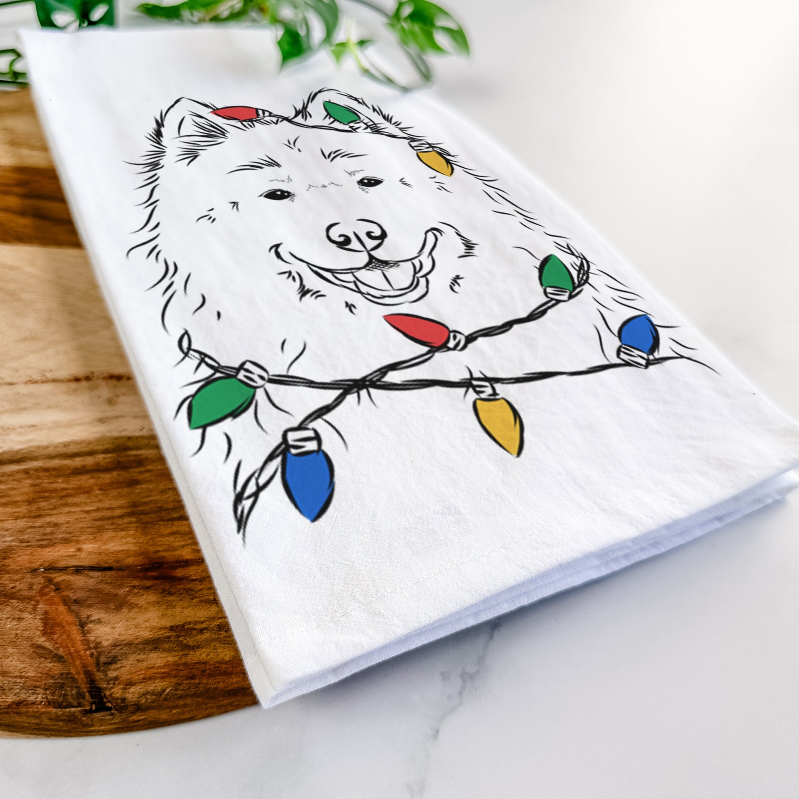 Hand-drawn sketch of Luka the Samoyed wrapped in Christmas lights on a tea towel