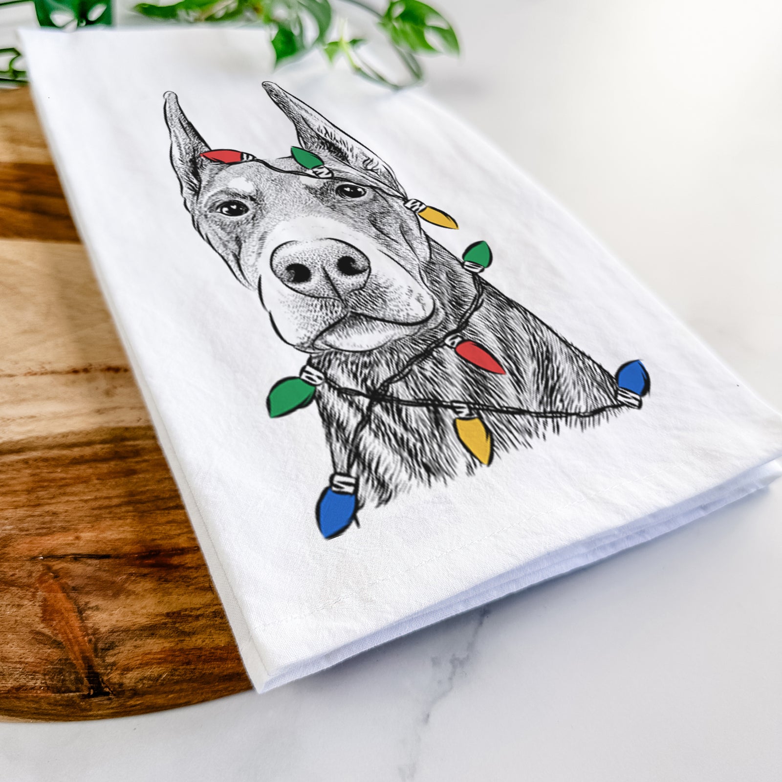 Hand-drawn sketch of Luna the Doberman Pinscher wrapped in Christmas lights on a tea towel