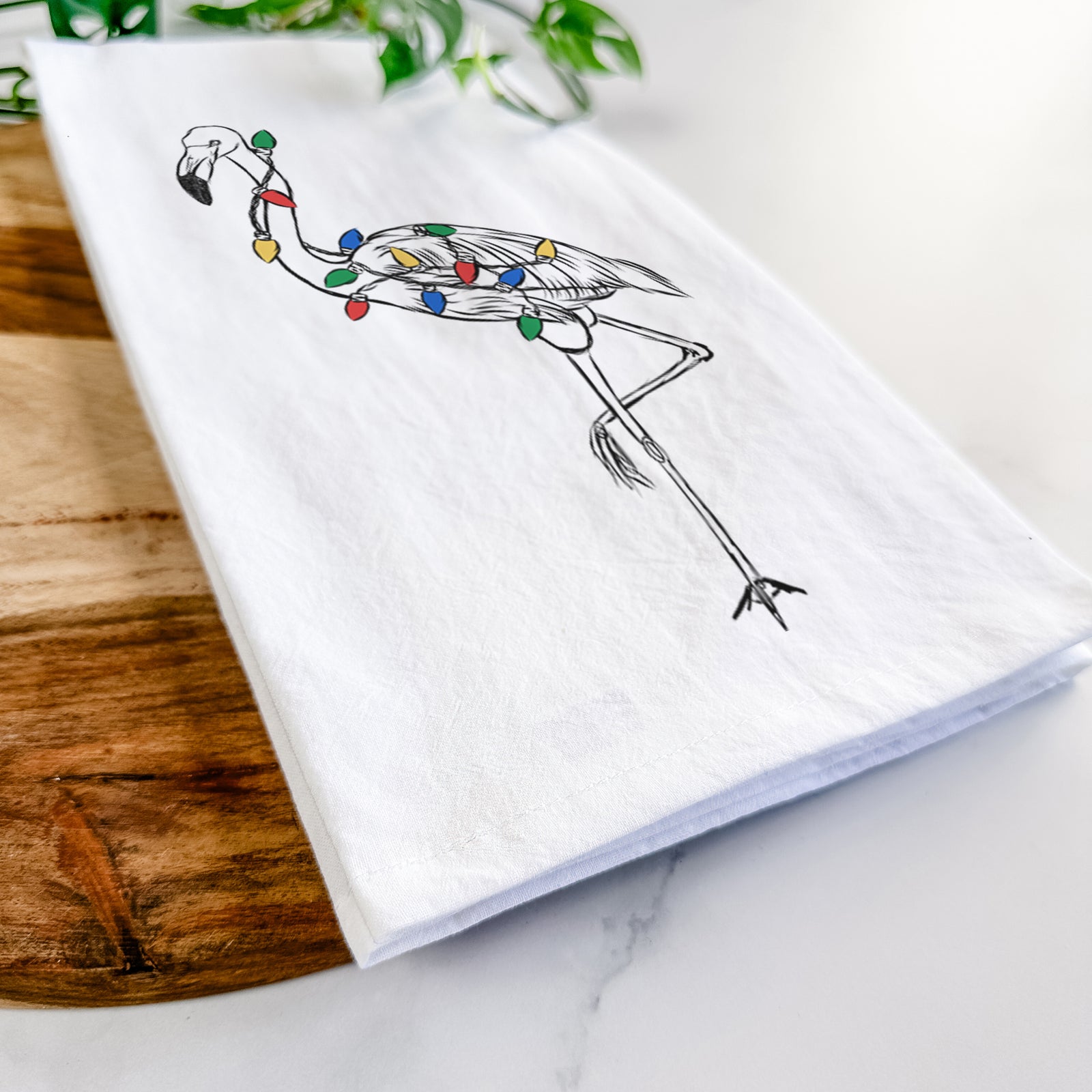 Hand-drawn sketch of Mango the Flamingo wrapped in Christmas lights on a tea towel