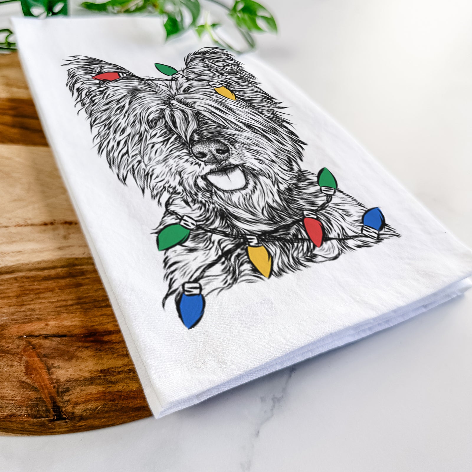 Hand-drawn sketch of McDuff the Cairn Terrier wrapped in Christmas lights on a tea towel