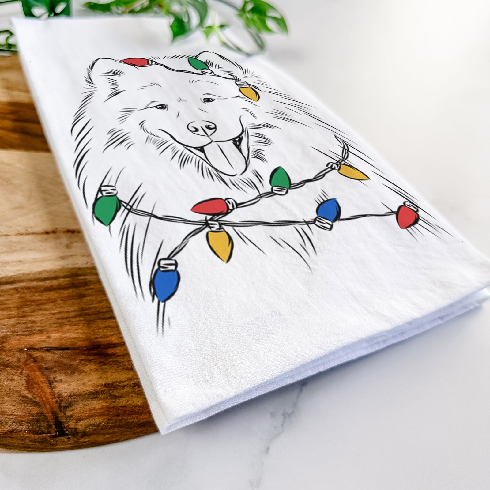 Hand-drawn sketch of Mikko the Samoyed wrapped in Christmas lights on a tea towel