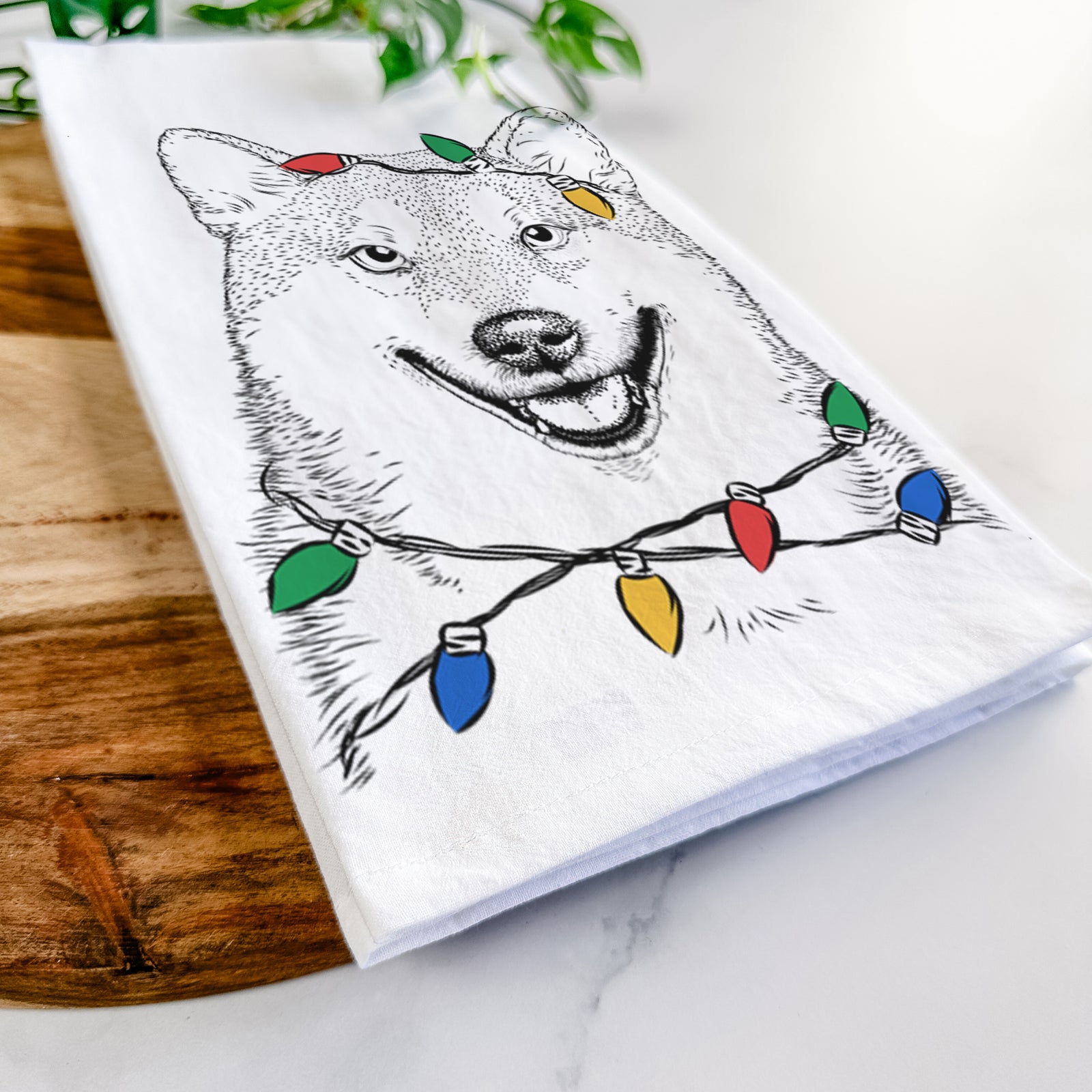 Hand-drawn sketch of Mitsu the Shiba Inu wrapped in Christmas lights on a tea towel