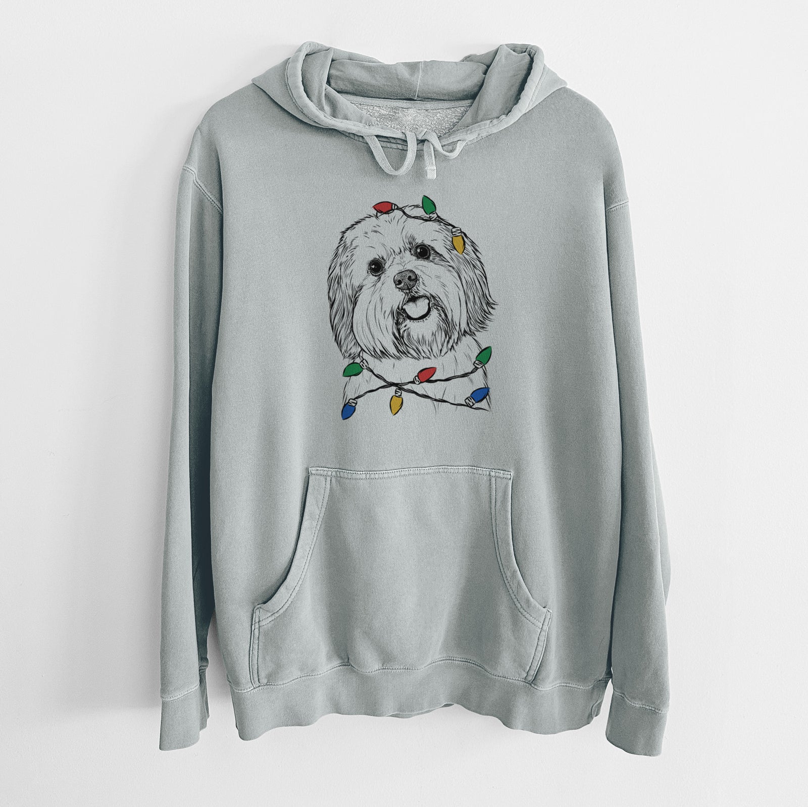 Hand-drawn sketch of Nikka the Lowchen wrapped in Christmas lights on a Sage Unisex pigment dyed hoodie
