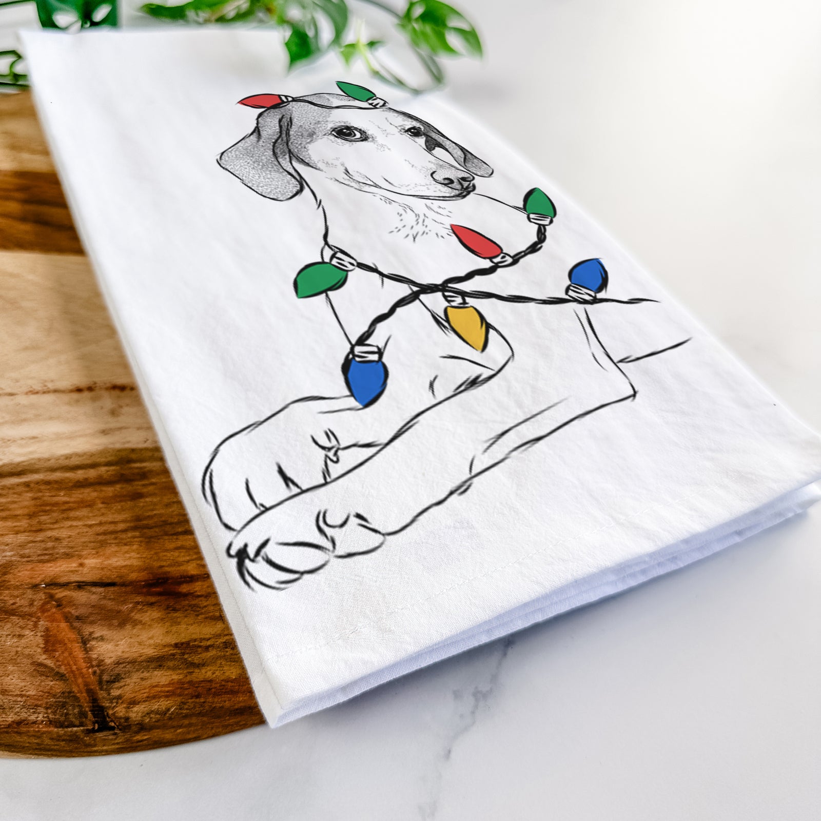 Hand-drawn sketch of Opie the Foxhound wrapped in Christmas lights on a tea towel