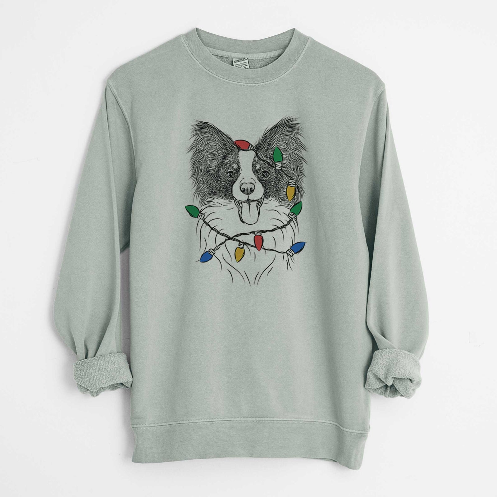 Hand-drawn sketch of Patrick the Papillon wrapped in Christmas lights on a Sage Unisex pigment dyed crew sweatshirt