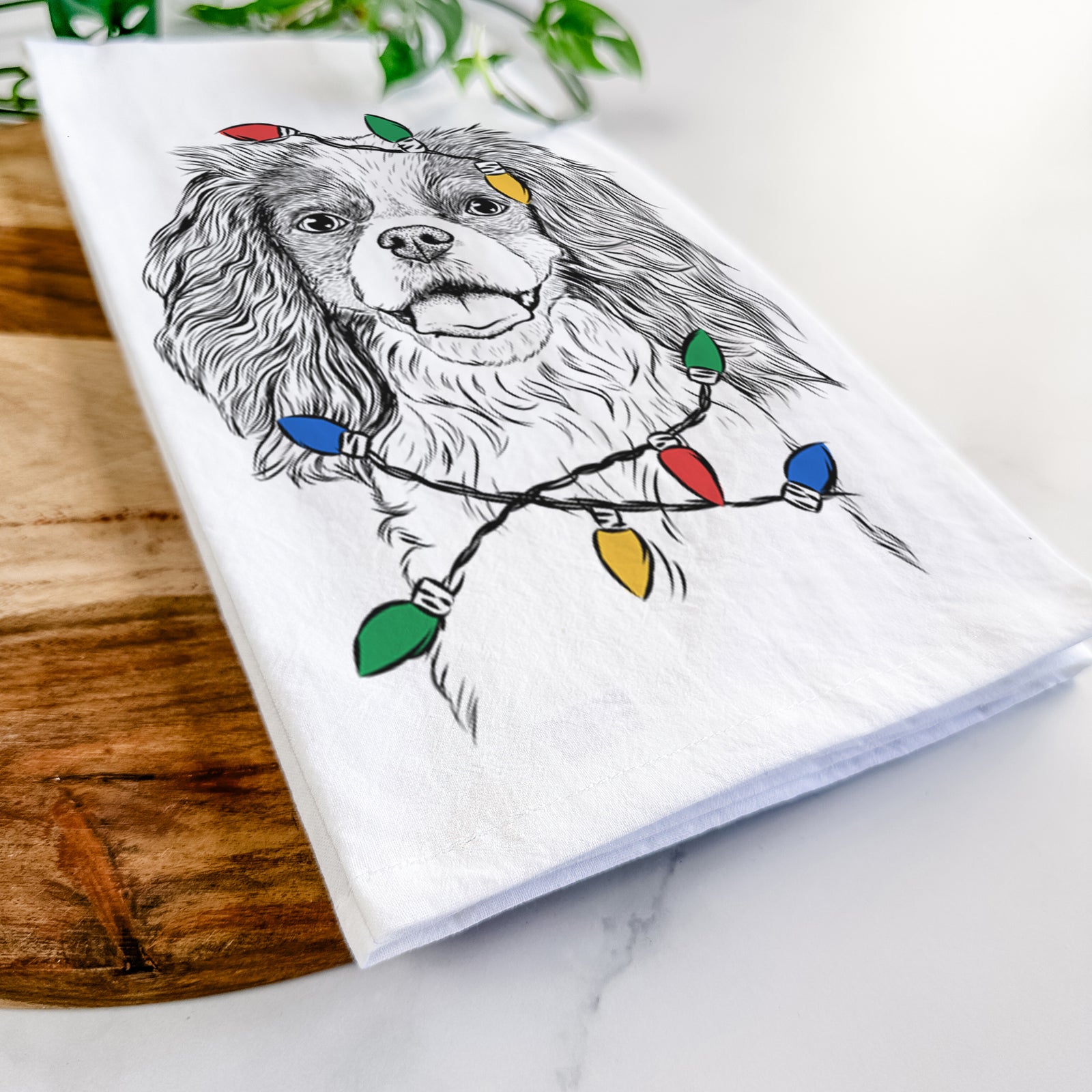 Hand-drawn sketch of Poppy the Cavalier King Charles Spaniel wrapped in Christmas lights on a tea towel