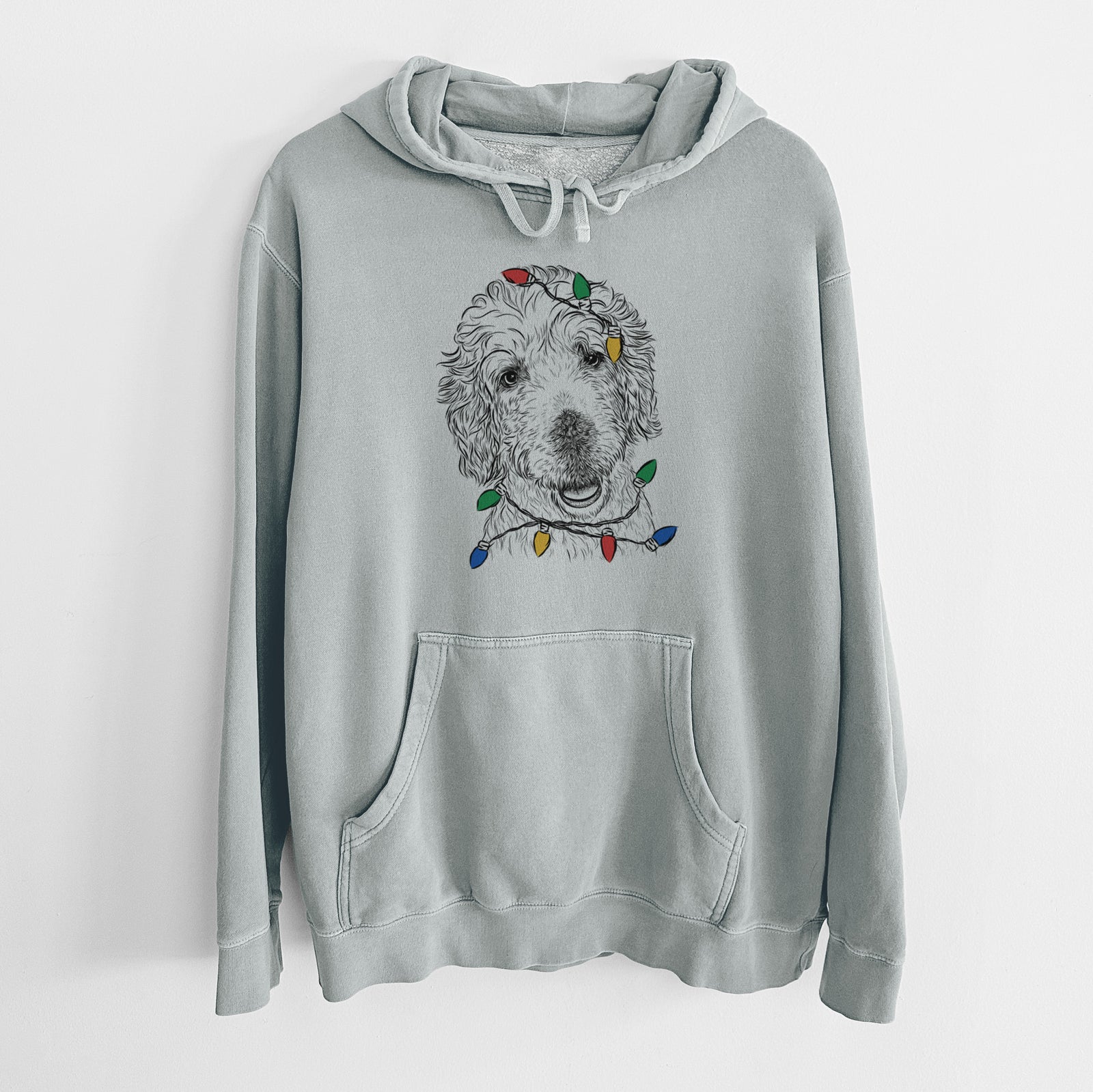 Hand-drawn sketch of Preston the Labradoodle wrapped in Christmas lights on a Sage Unisex pigment dyed hoodie