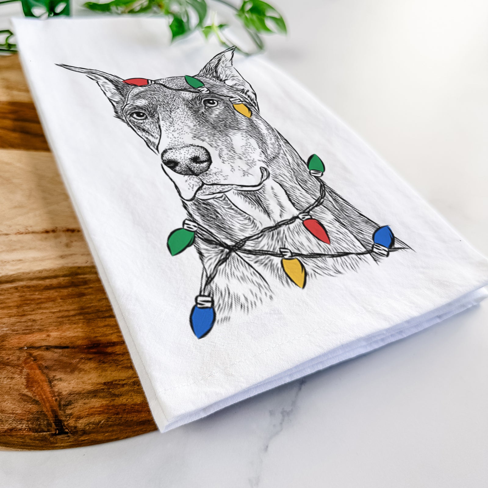 Hand-drawn sketch of RJ the Doberman Pinscher wrapped in Christmas lights on a tea towel