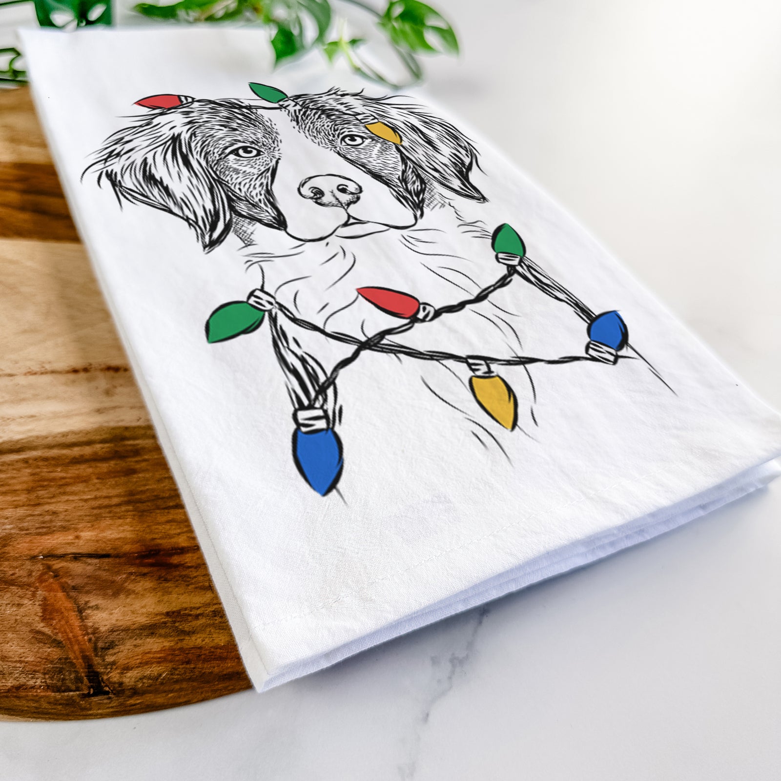 Hand-drawn sketch of Remi the Brittany wrapped in Christmas lights on a tea towel