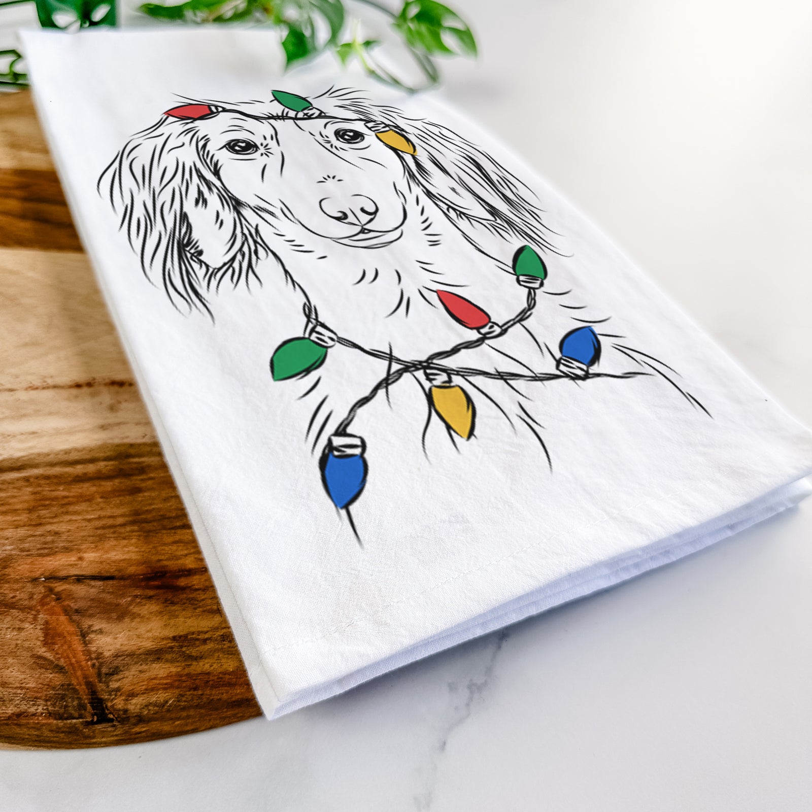 Hand-drawn sketch of Roux the Long Haired Dachshund wrapped in Christmas lights on a tea towel