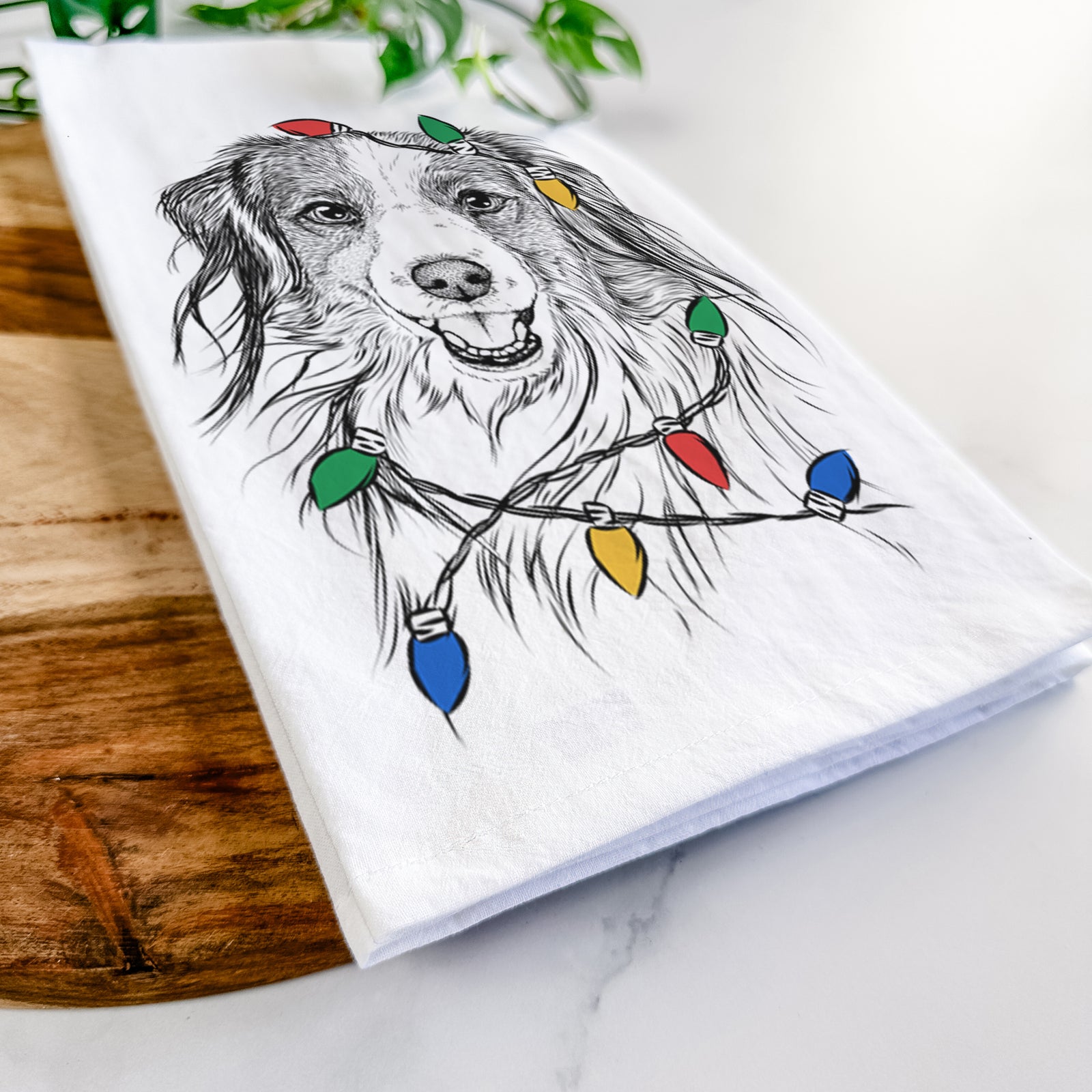 Hand-drawn sketch of Rutger the Nederlandse Kooikerhondje wrapped in Christmas lights on a tea towel