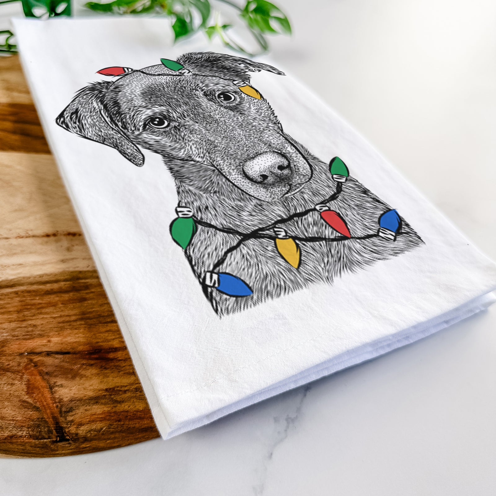 Hand-drawn sketch of Sadie the Whipador wrapped in Christmas lights on a tea towel