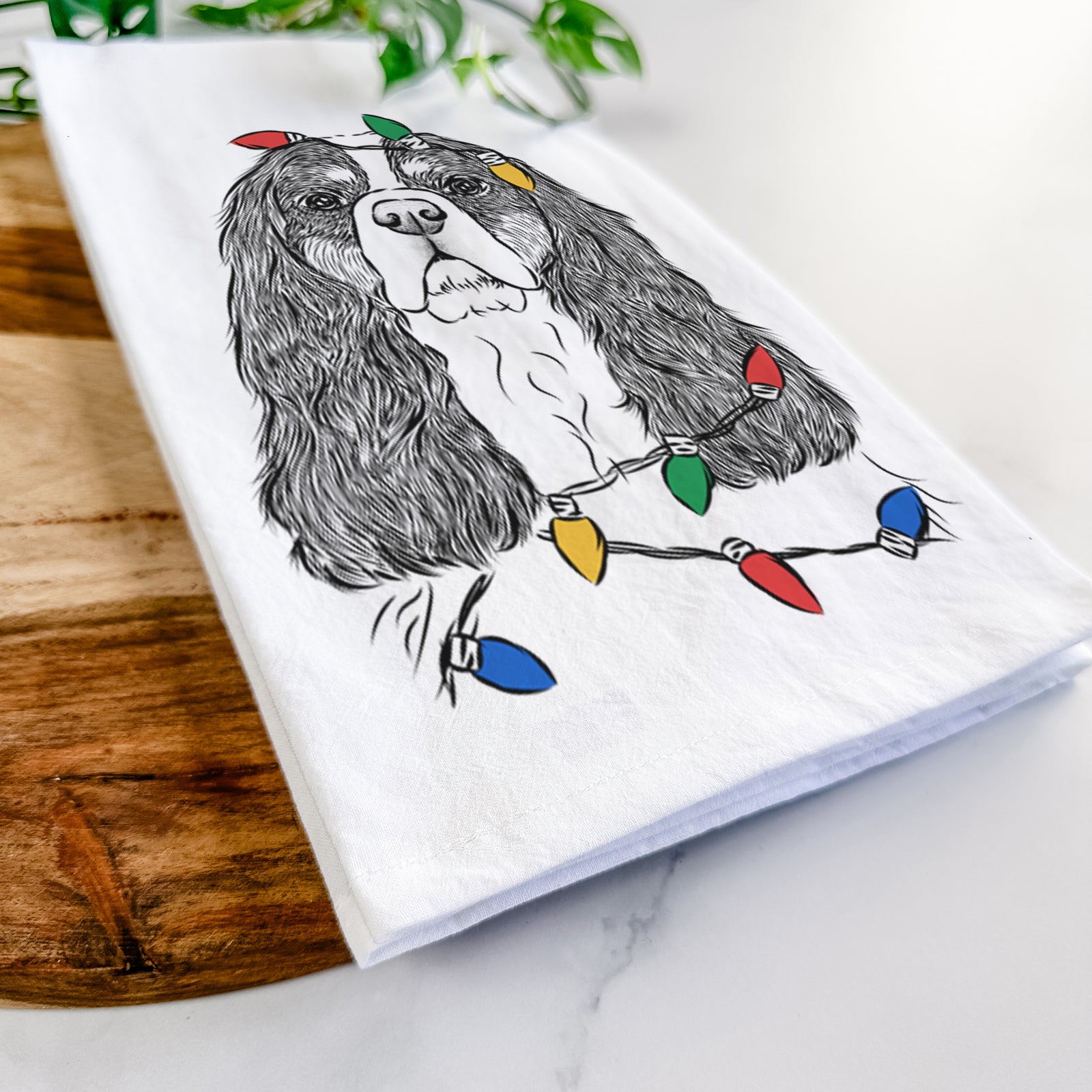 Hand-drawn sketch of Sebastian the Cavalier King Charles Spaniel wrapped in Christmas lights on a tea towel