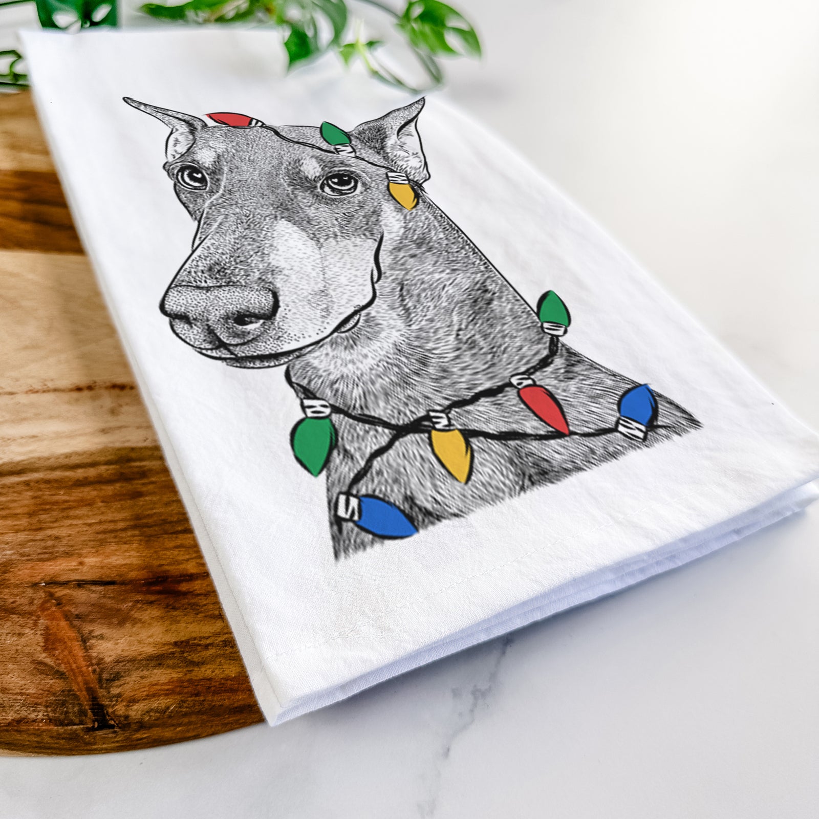 Hand-drawn sketch of Shelby the Doberman Pinscher wrapped in Christmas lights on a tea towel
