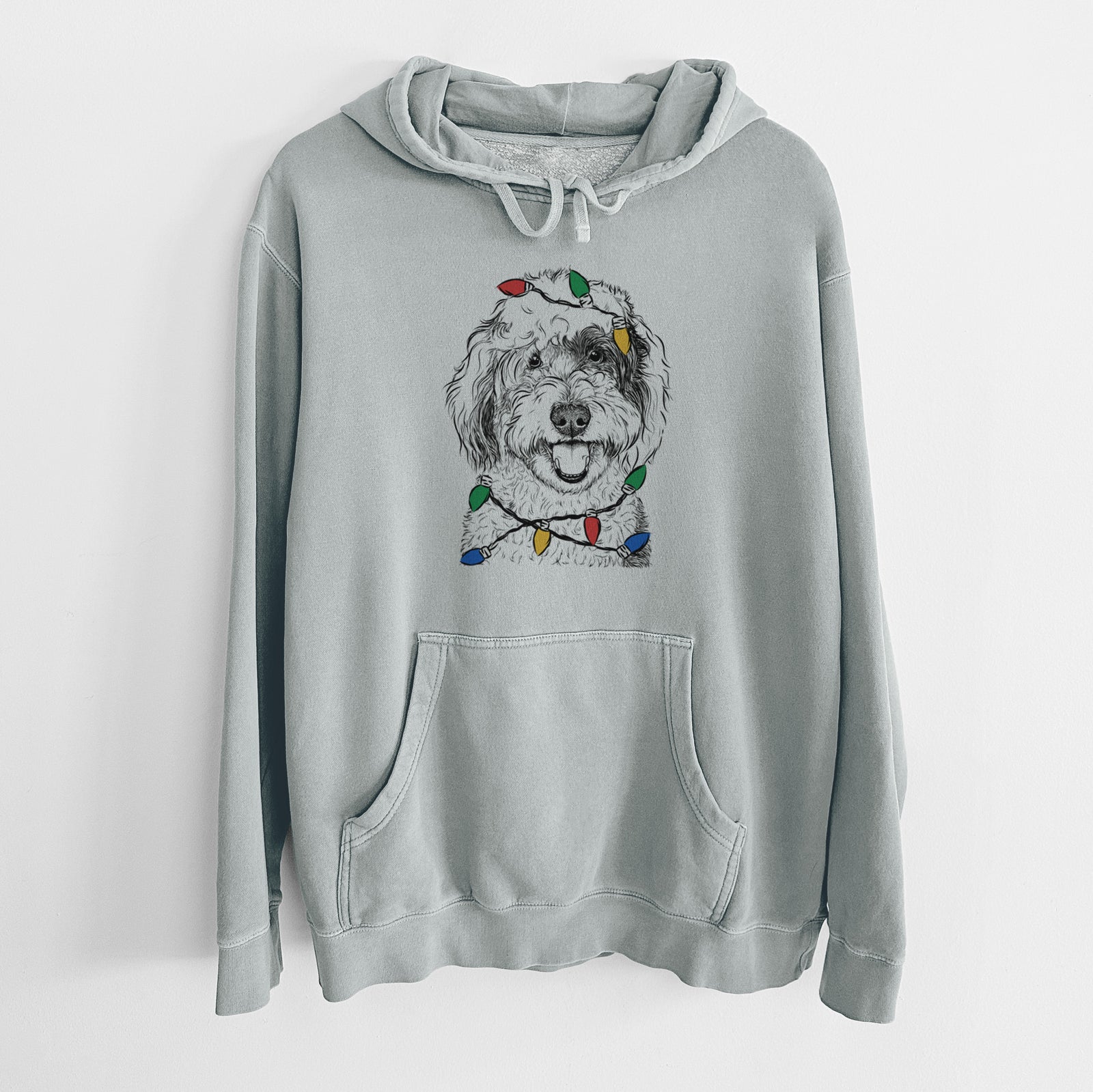 Hand-drawn sketch of Sherlock the Sheepadoodle wrapped in Christmas lights on a Sage Unisex pigment dyed hoodie