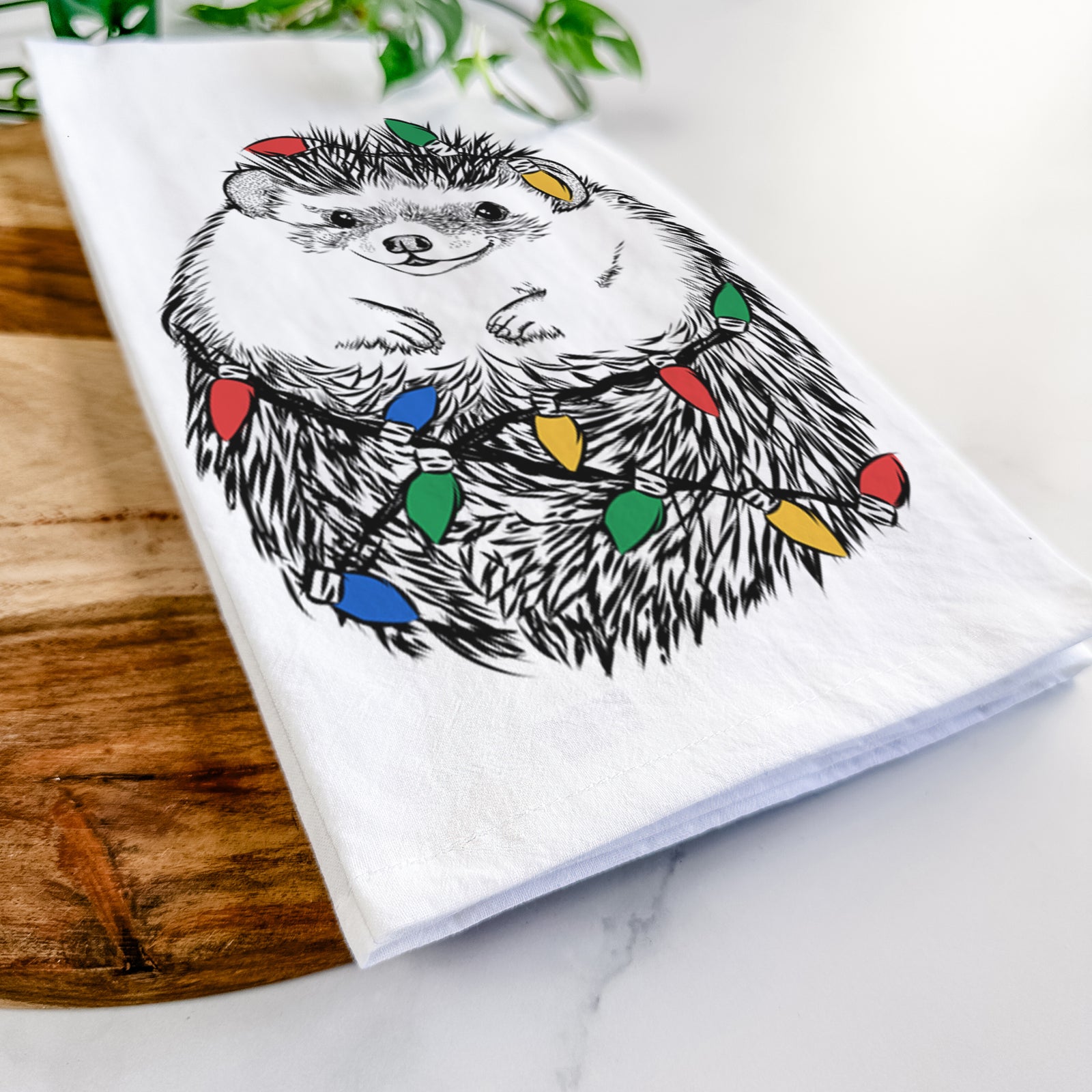 Hand-drawn sketch of Sid the Hedgehog wrapped in Christmas lights on a tea towel
