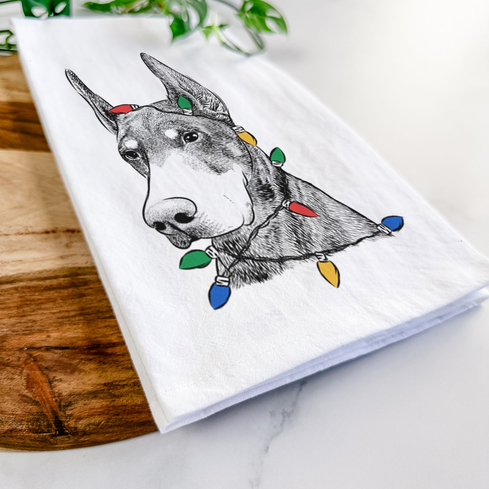 Hand-drawn sketch of Sunny the Doberman Pinscher wrapped in Christmas lights on a tea towel