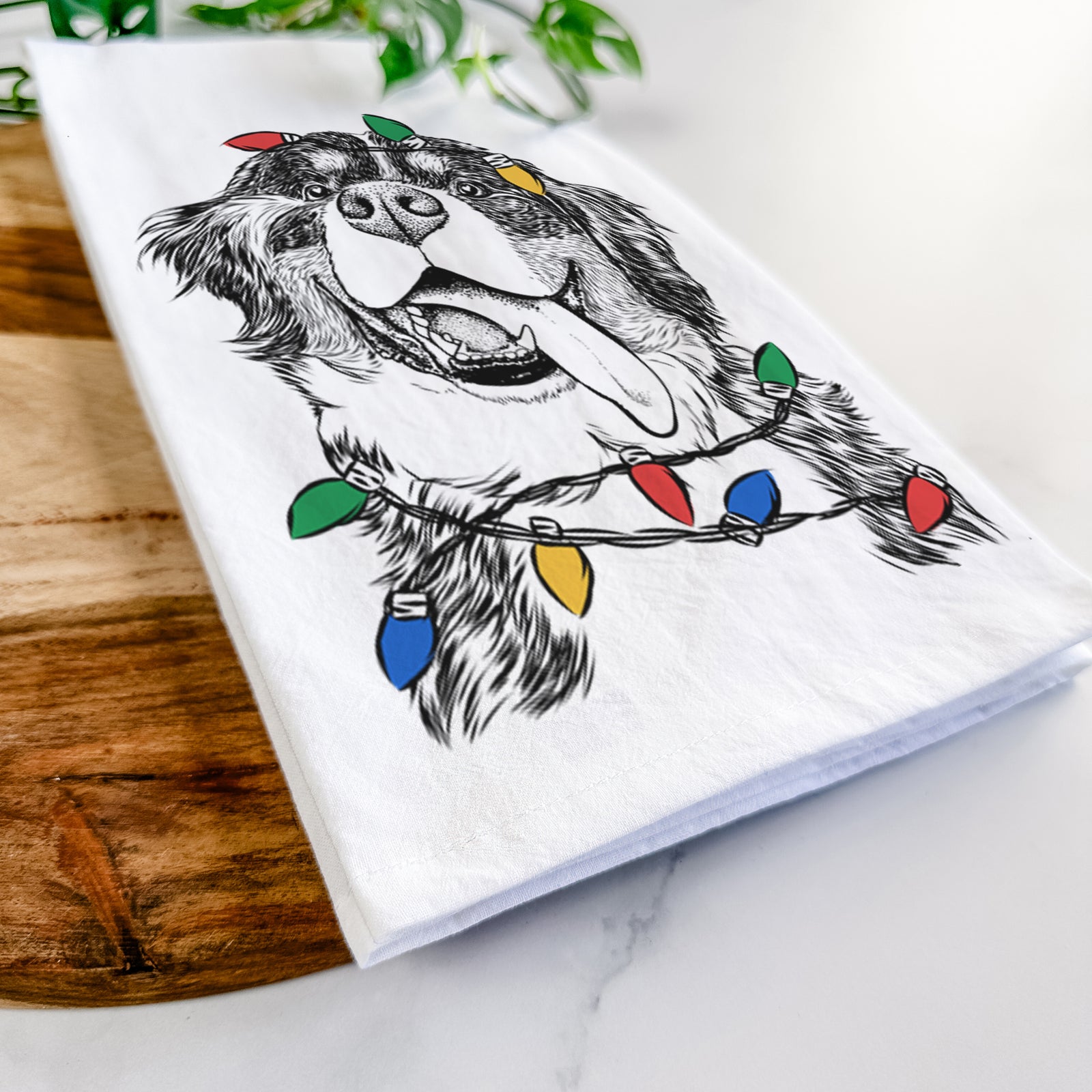Hand-drawn sketch of Theo the Bernese Mountain Dog wrapped in Christmas lights on a tea towel