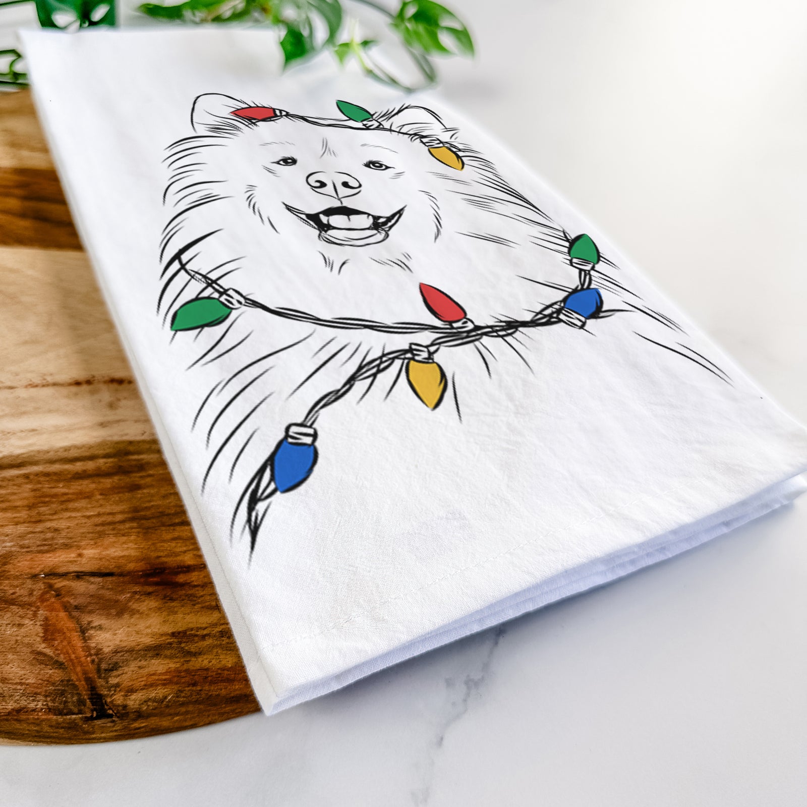 Hand-drawn sketch of Tillie the Samoyed wrapped in Christmas lights on a tea towel