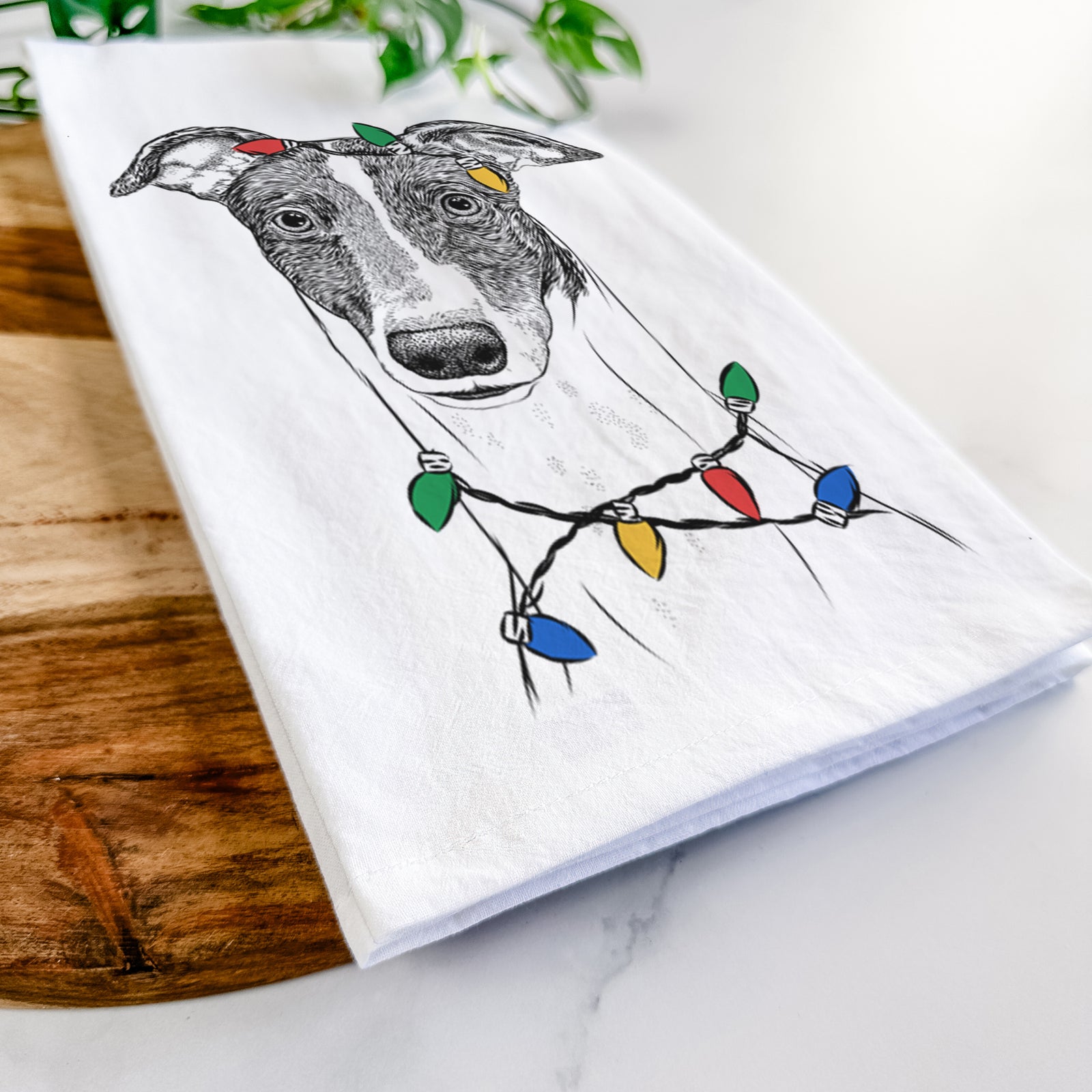 Hand-drawn sketch of Vyncent the Greyhound wrapped in Christmas lights on a tea towel