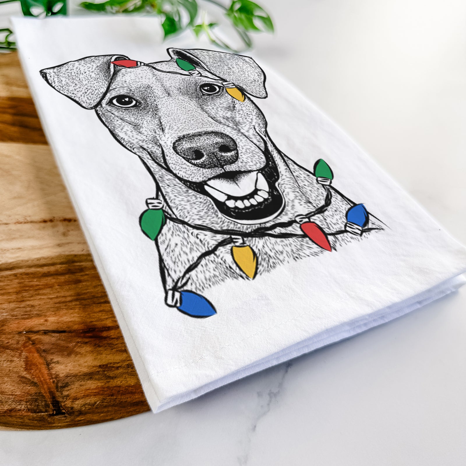 Hand-drawn sketch of Willow the German Pinscher wrapped in Christmas lights on a tea towel