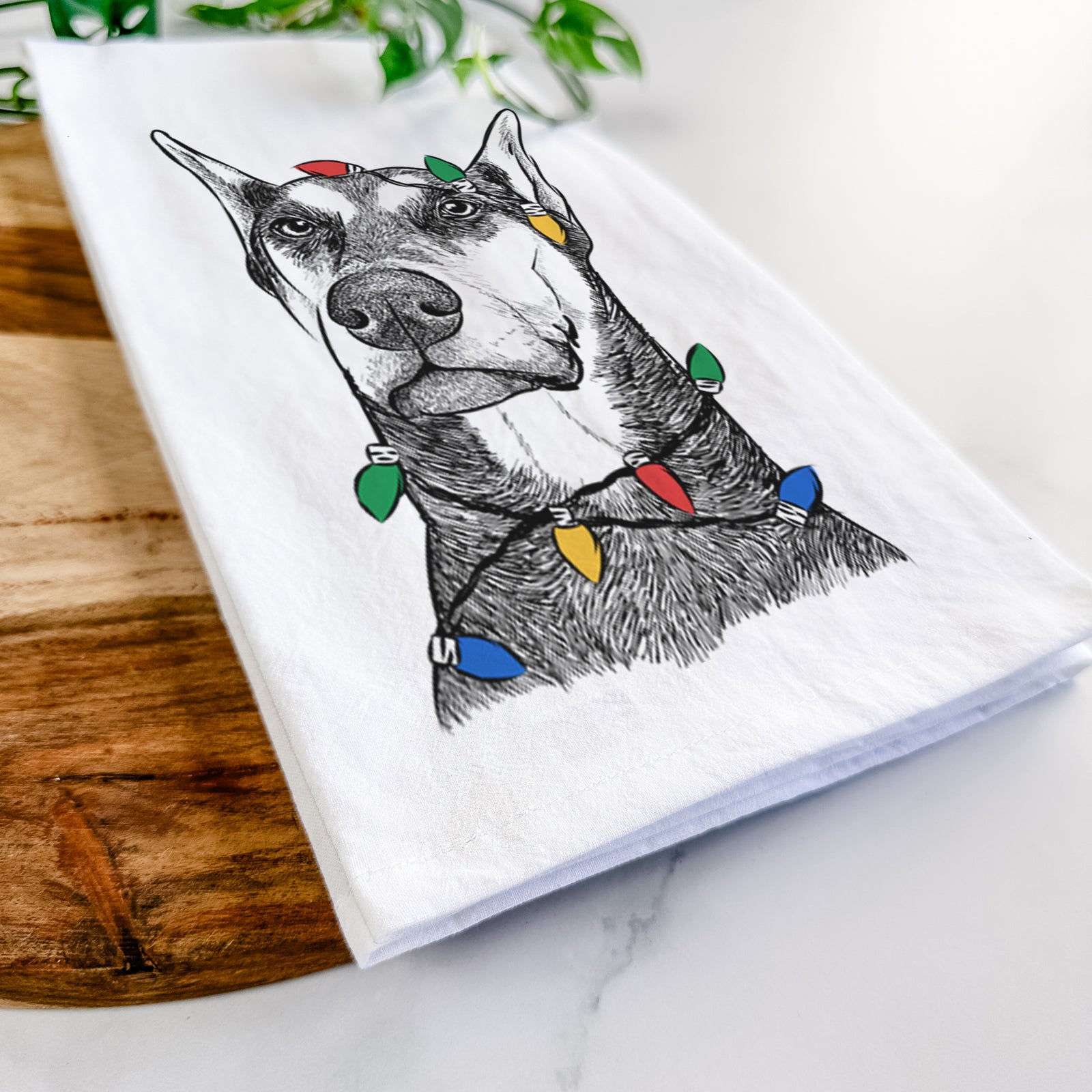 Hand-drawn sketch of Zeus the Doberman Pinscher wrapped in Christmas lights on a tea towel