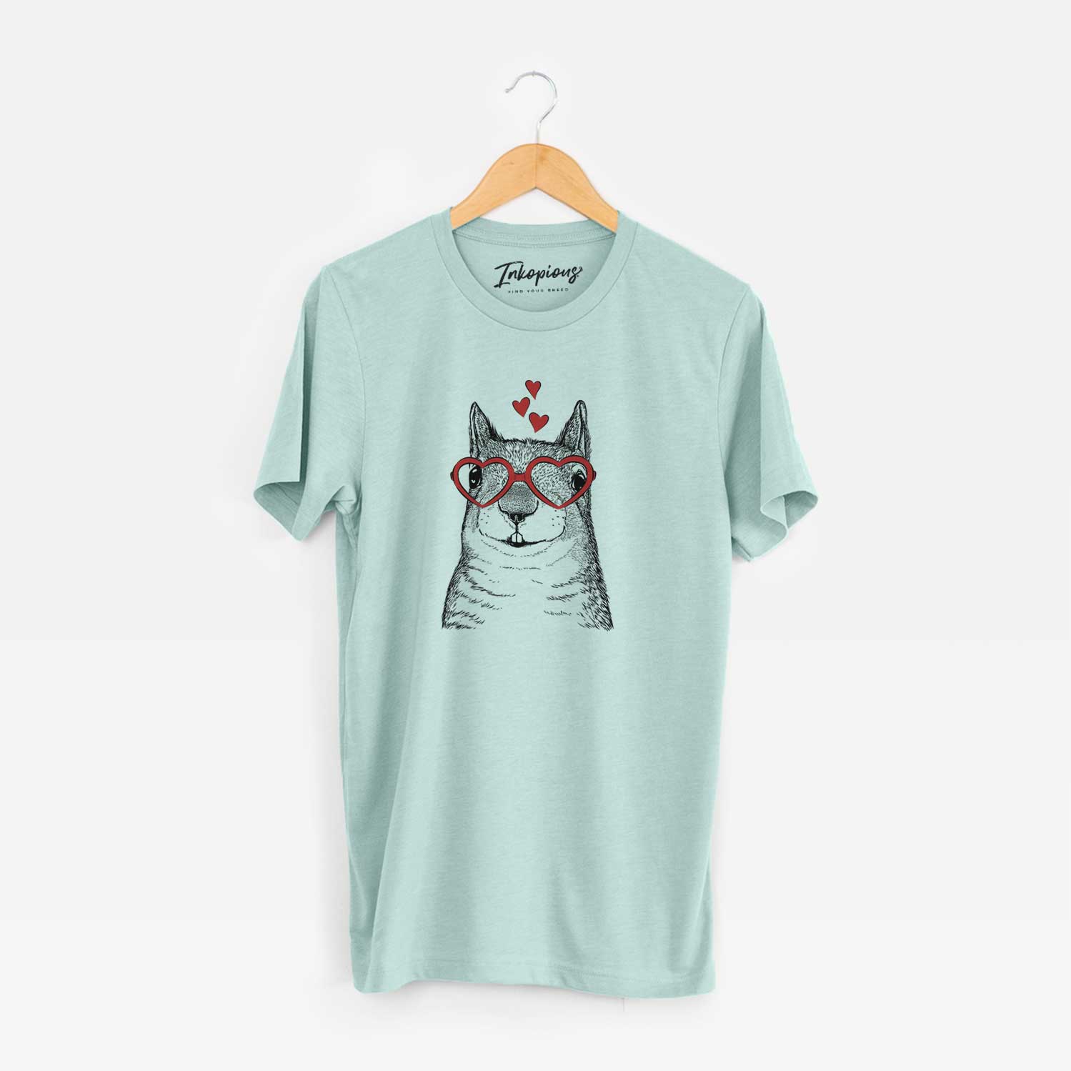 Hand-drawn sketch of Nibbles the Squirrel wearing heart-shaped glasses on a Heather Sage Unisex crewneck