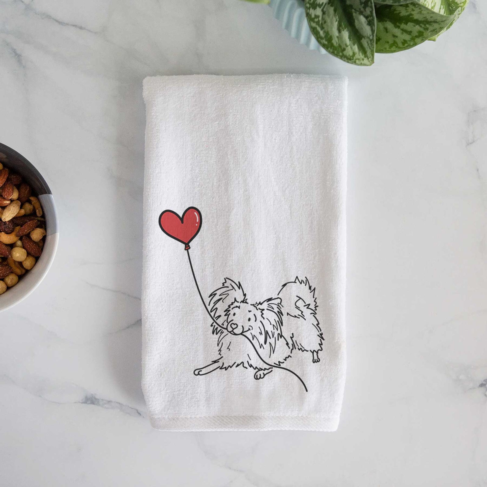 Minimalist line drawing of a Papillon Heart String holding a heart balloon on a decorative hand towel