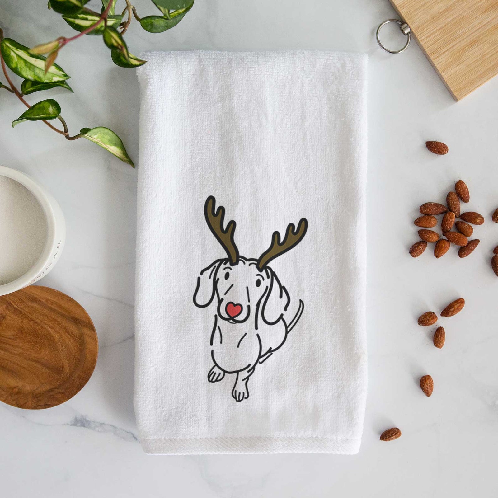 Minimalist line drawing of Moxie the Dachshund with reindeer antlers and a red nose on a decorative hand towel