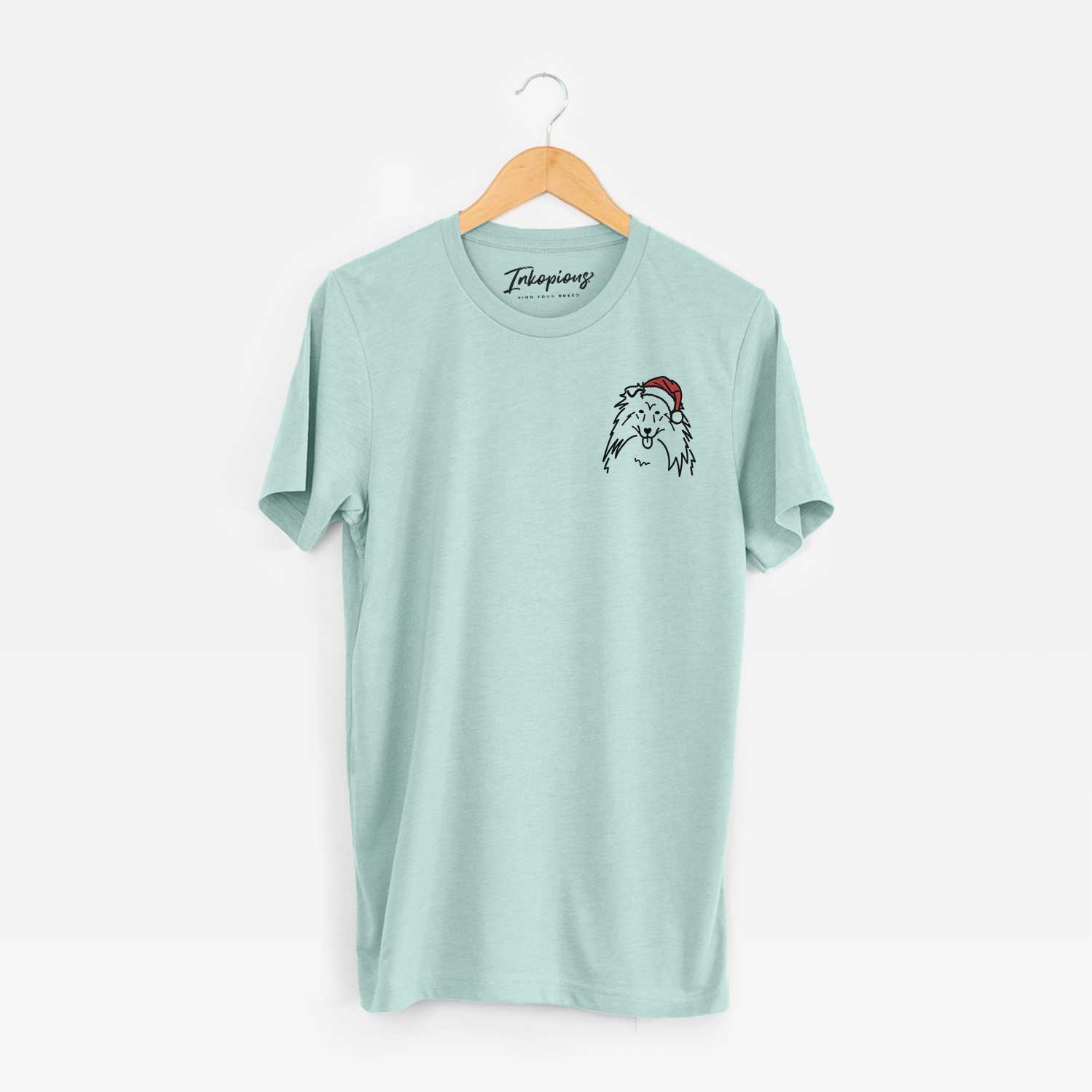 Small chest-pocket minimalist line drawing of a Rough Collie wearing a Santa hat on a Heather Sage Unisex crewneck