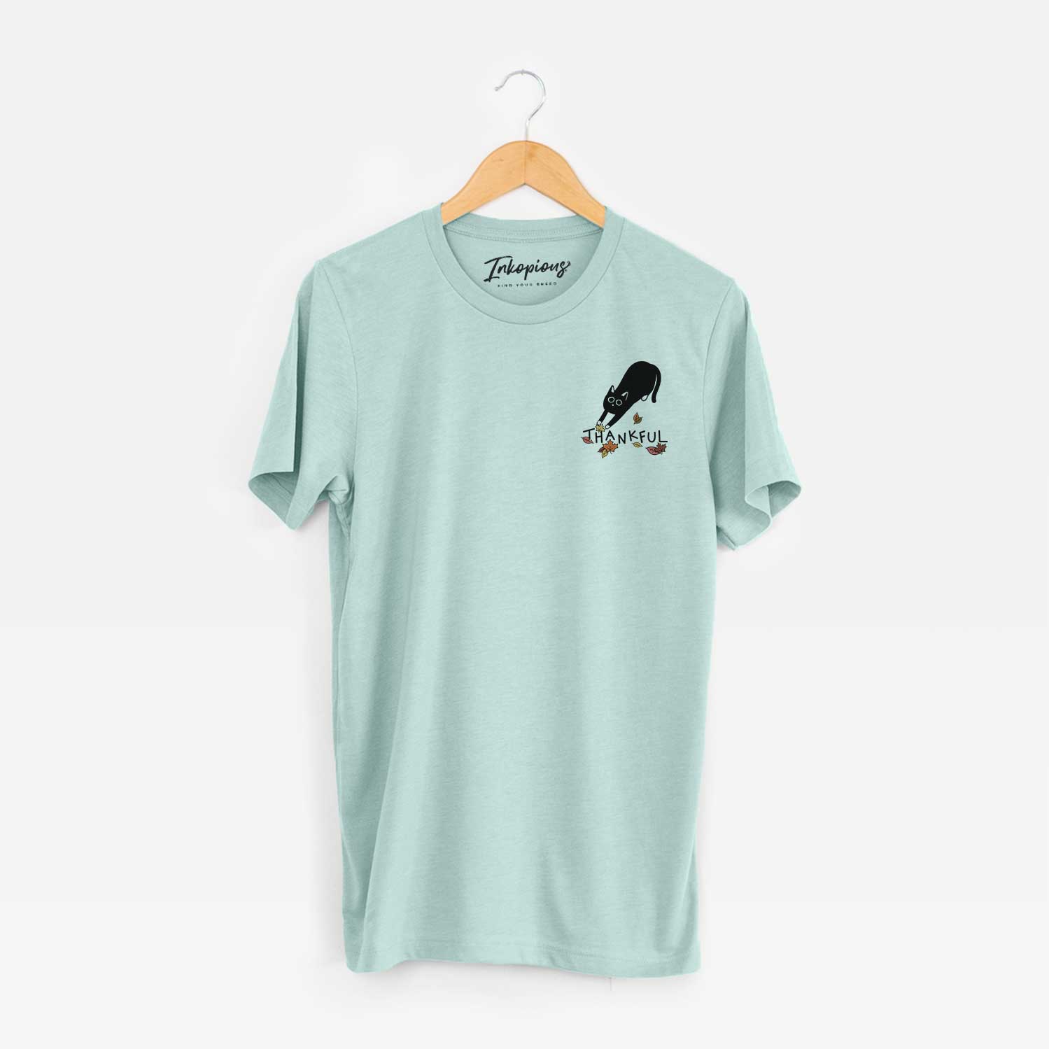 Small chest-pocket minimalist line drawing of Bug the Black Cat with 'Thankful' lettering on a Heather Sage Unisex crewneck