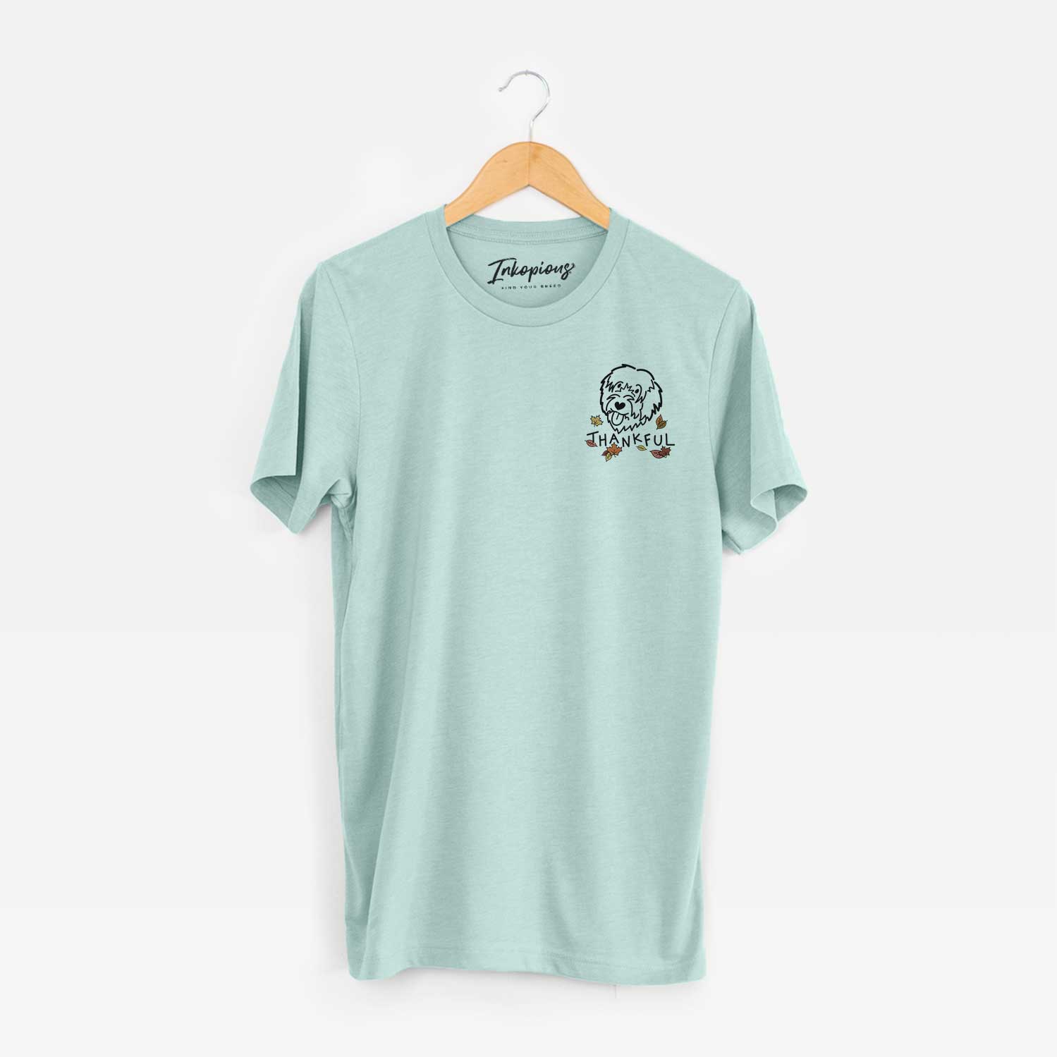 Small chest-pocket minimalist line drawing of a Catalan Sheepdog with 'Thankful' lettering on a Heather Sage Unisex crewneck