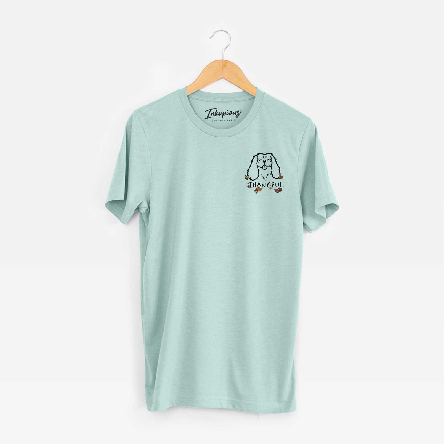 Small chest-pocket minimalist line drawing of a Cavalier King Charles Spaniel with 'Thankful' lettering on a Heather Sage Unisex crewneck