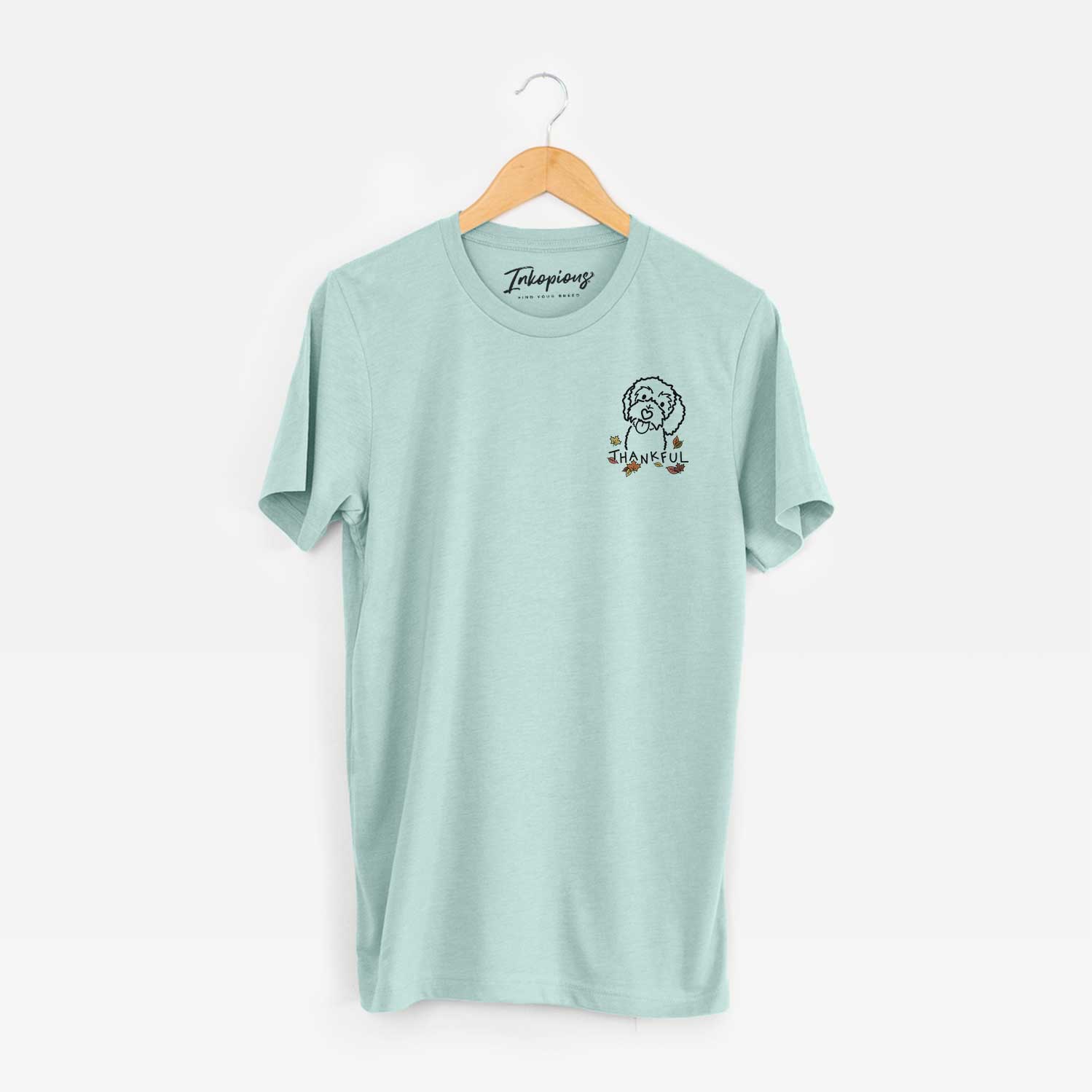 Small chest-pocket minimalist line drawing of Mabel the Bernedoodle with 'Thankful' lettering on a Heather Sage Unisex crewneck
