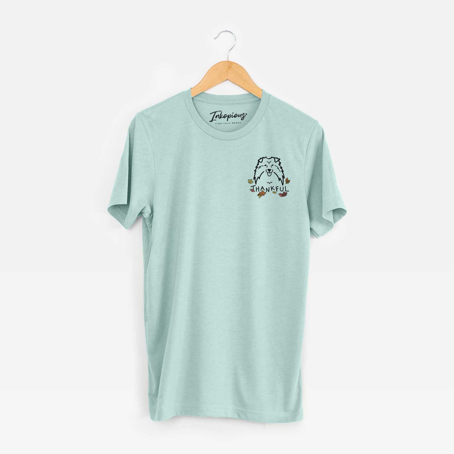 Small chest-pocket minimalist line drawing of a Shetland Sheepdog with 'Thankful' lettering on a Heather Sage Unisex crewneck