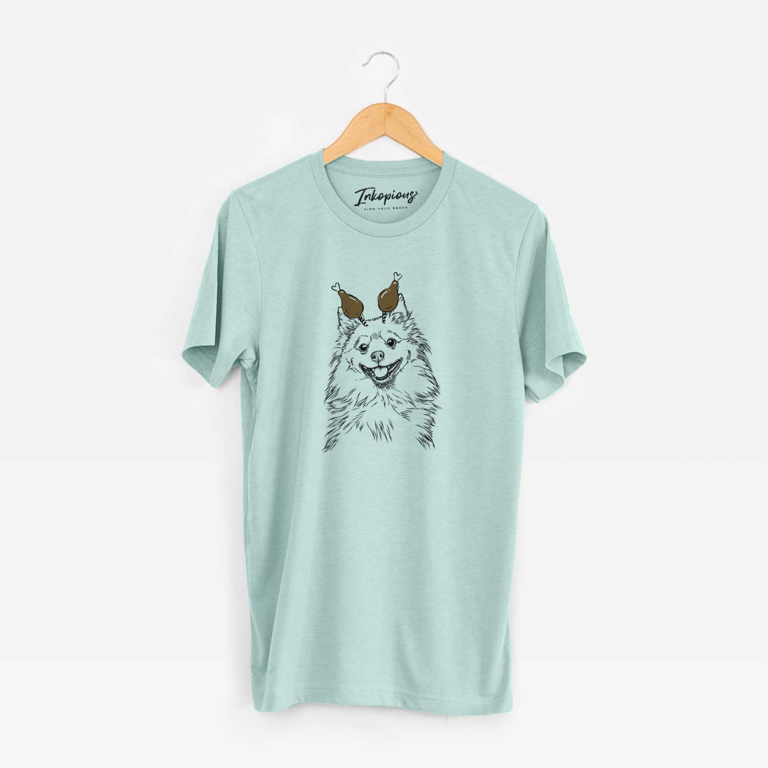 Hand-drawn sketch of Fibi the Spitz with a Thanksgiving turkey headpiece on a Heather Sage Unisex crewneck