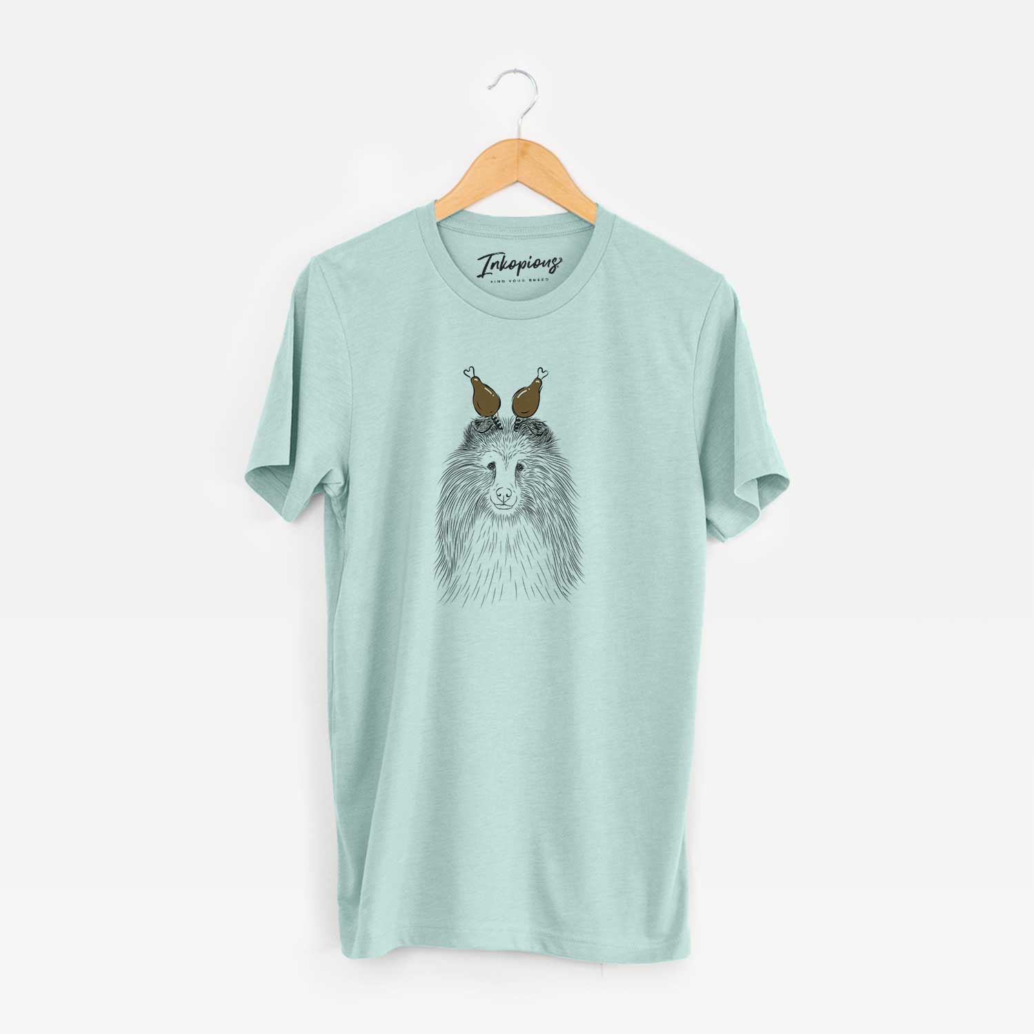Hand-drawn sketch of Moxie the Shetland Sheepdog with a Thanksgiving turkey headpiece on a Heather Sage Unisex crewneck
