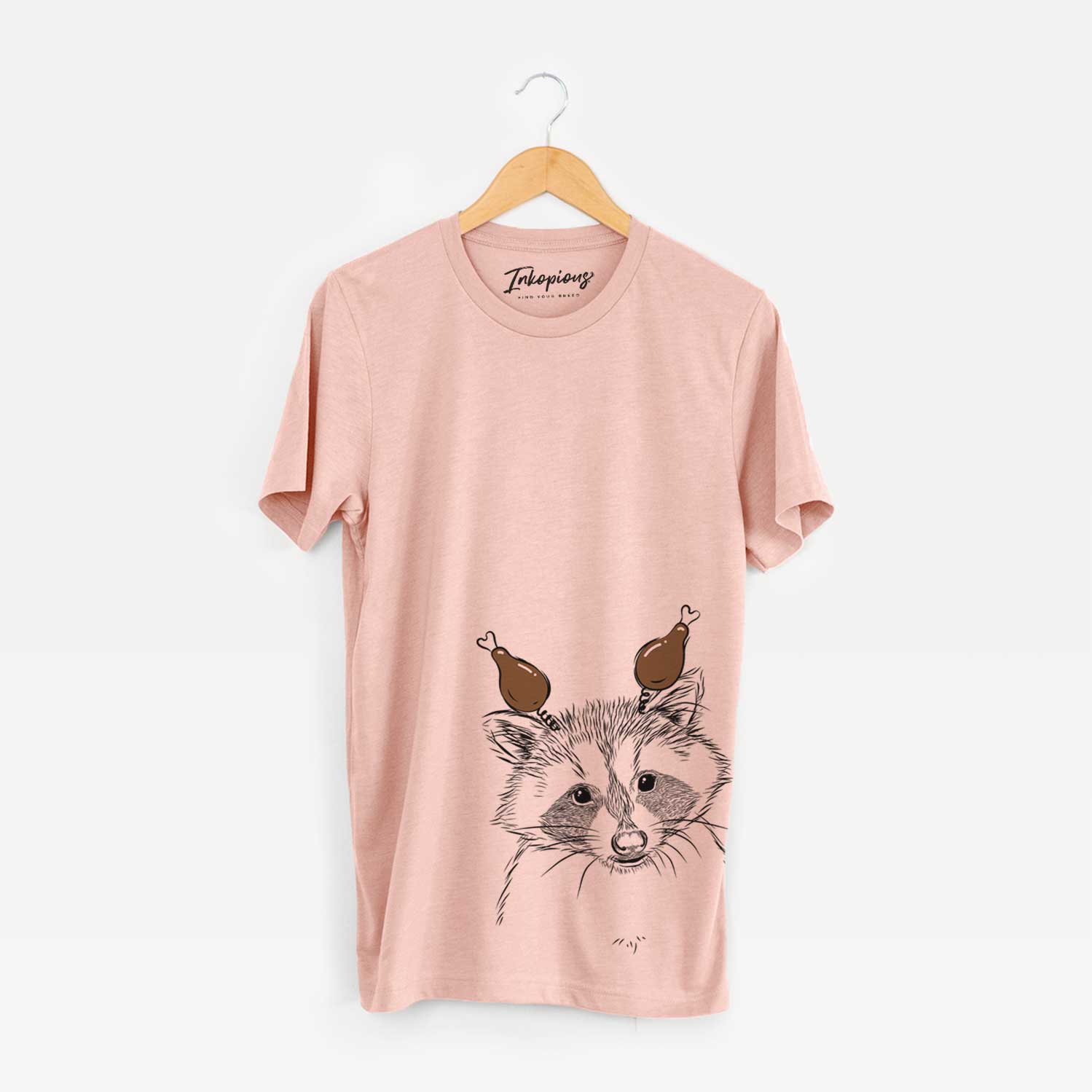 Hand-drawn sketch of Randy the Raccoon with a Thanksgiving turkey headpiece on a Peach Unisex crewneck