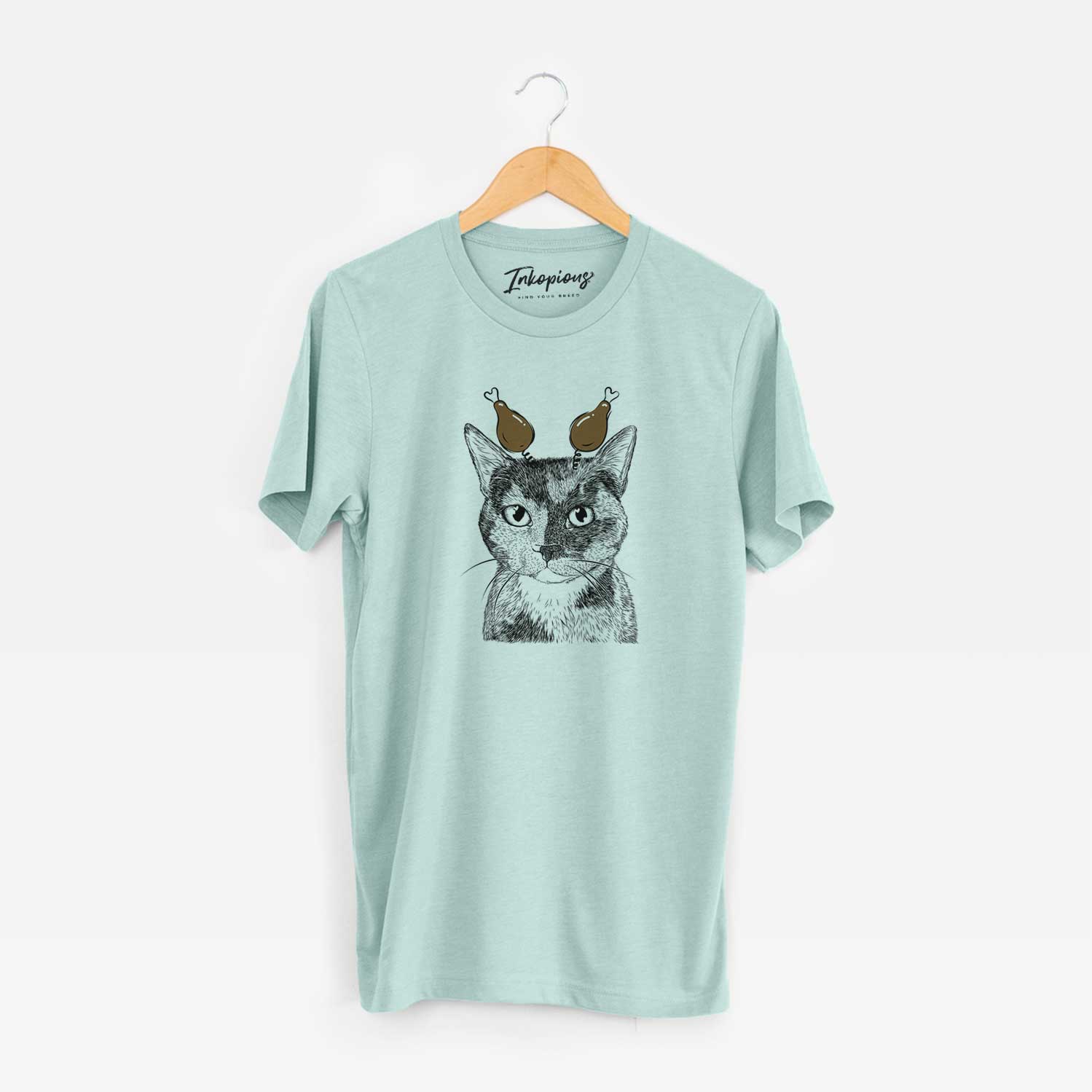 Hand-drawn sketch of Spooky Kitty the Tortoiseshell Cat with a Thanksgiving turkey headpiece on a Heather Sage Unisex crewneck