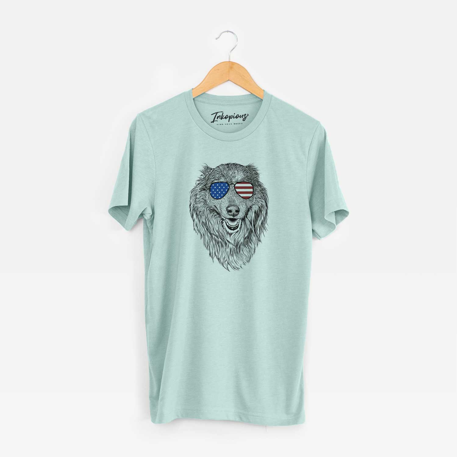 Hand-drawn sketch of Addie the Collie Mix wearing American flag sunglasses on a Heather Sage Unisex crewneck