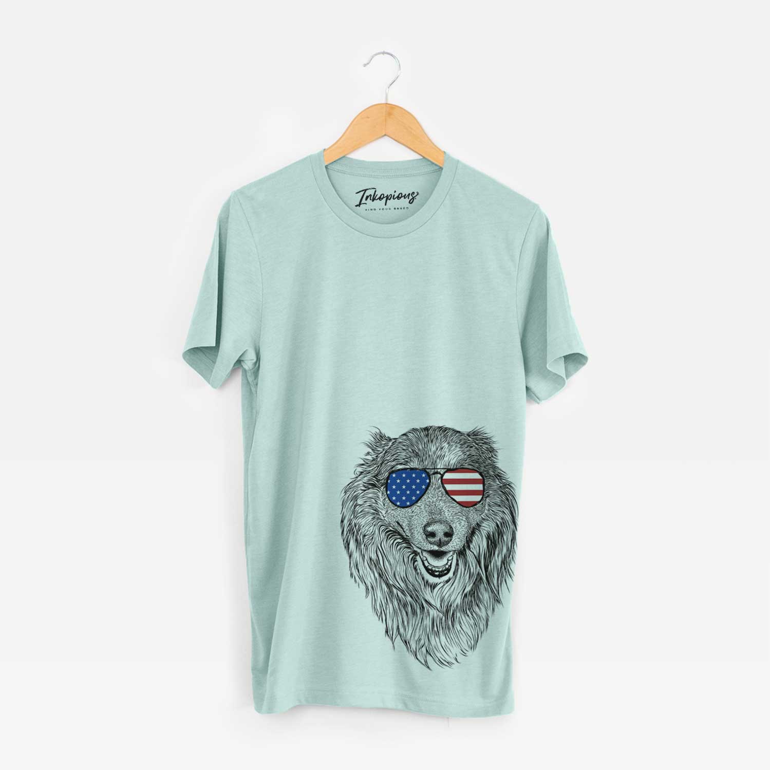 Hand-drawn sketch of Addie the Collie Mix wearing American flag sunglasses on a Heather Sage Unisex crewneck