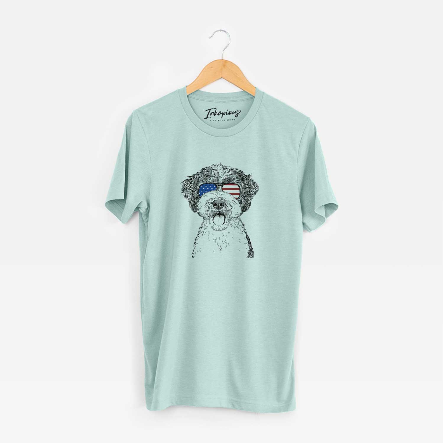 Hand-drawn sketch of Bella the Cockapoo wearing American flag sunglasses on a Heather Sage Unisex crewneck