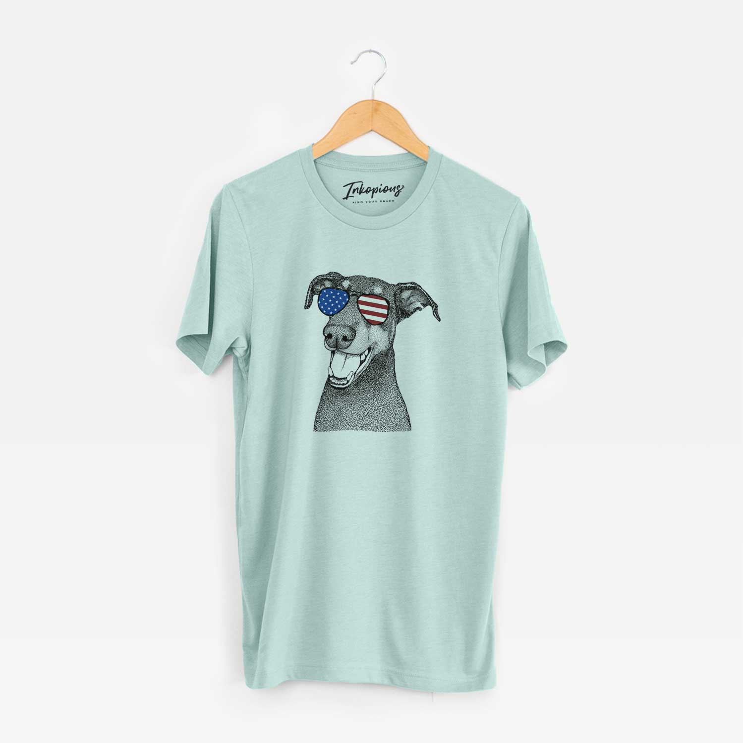Hand-drawn sketch of Bunnie the Doberman Pinscher wearing American flag sunglasses on a Heather Sage Unisex crewneck