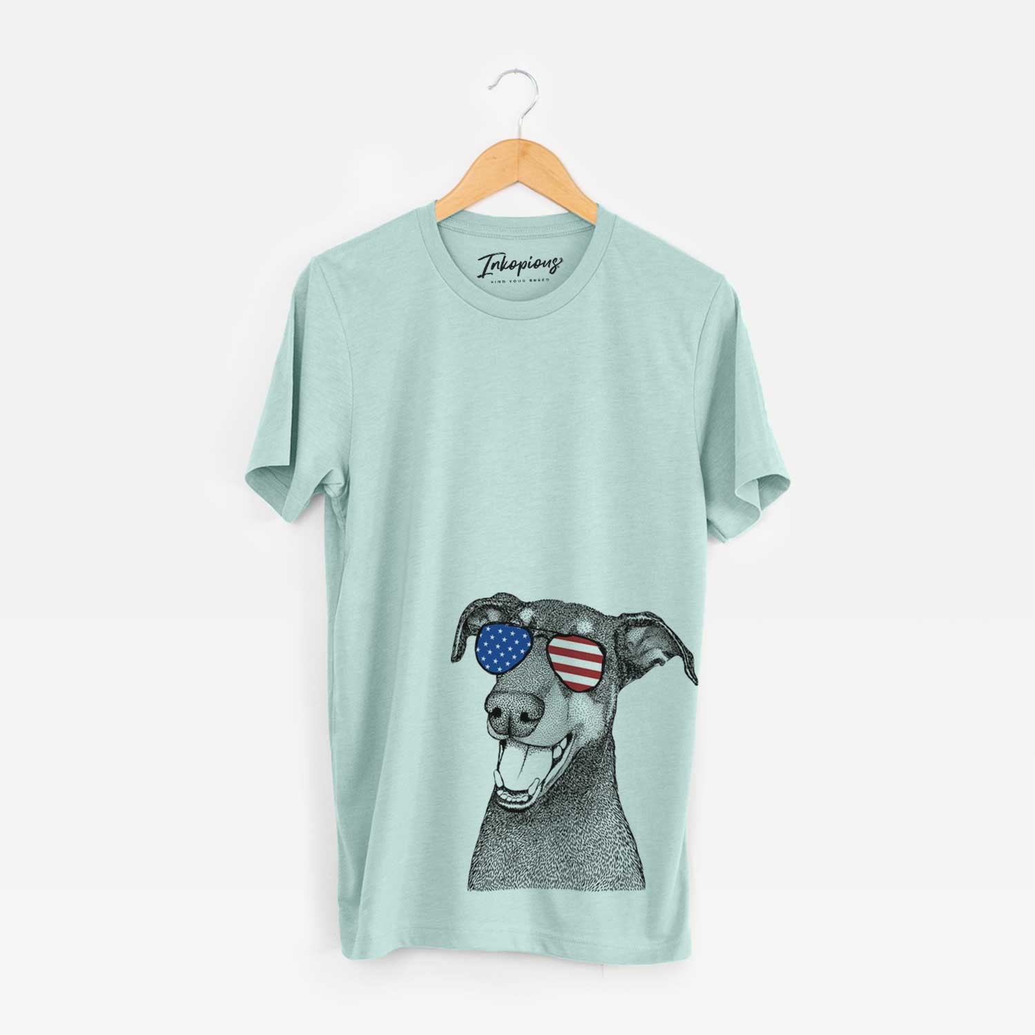 Hand-drawn sketch of Bunnie the Doberman Pinscher wearing American flag sunglasses on a Heather Sage Unisex crewneck