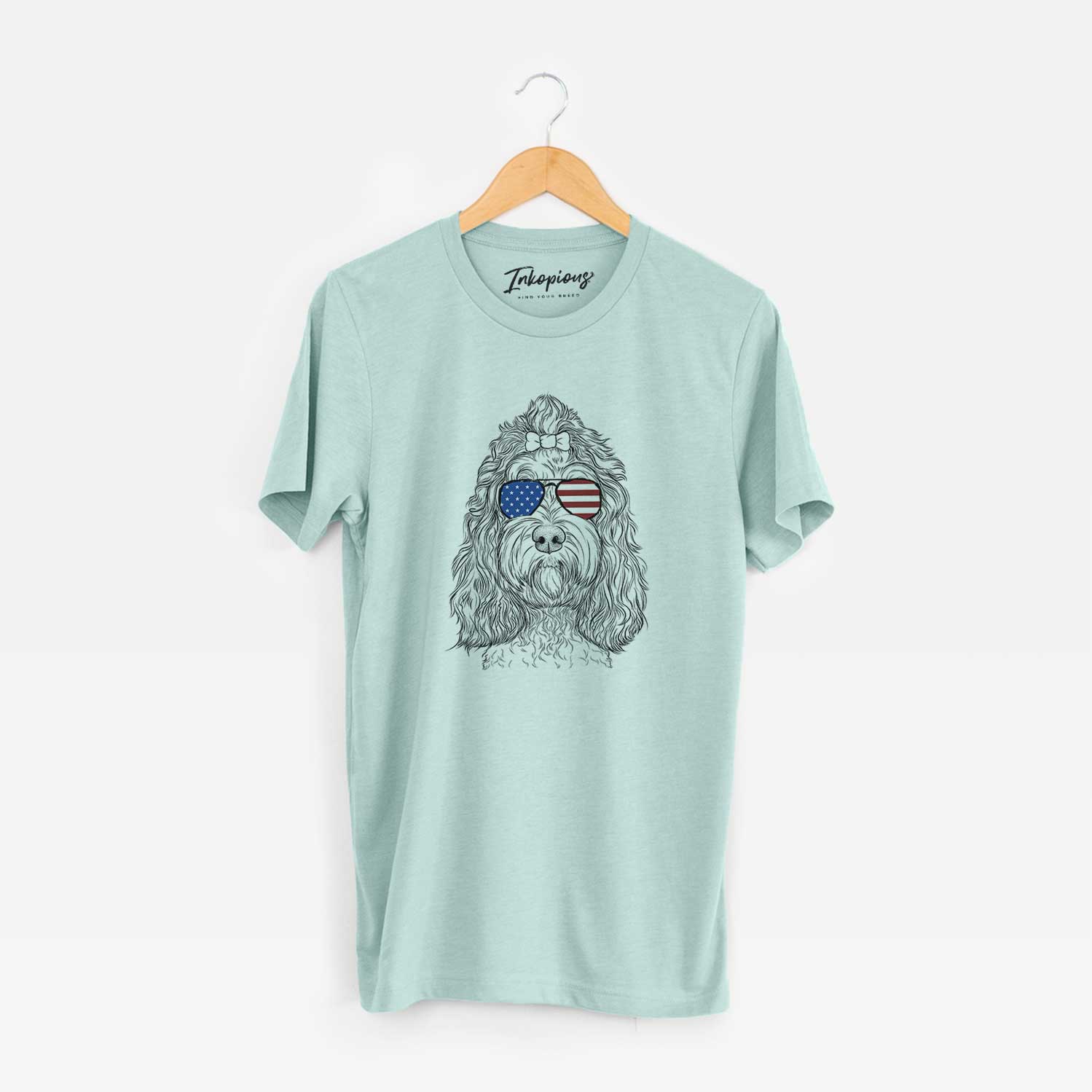 Hand-drawn sketch of Chloe the Cockapoo wearing American flag sunglasses on a Heather Sage Unisex crewneck