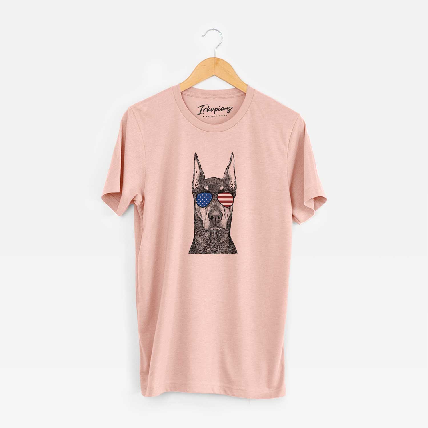 Hand-drawn sketch of Drake the Doberman Pinscher wearing American flag sunglasses on a Peach Unisex crewneck